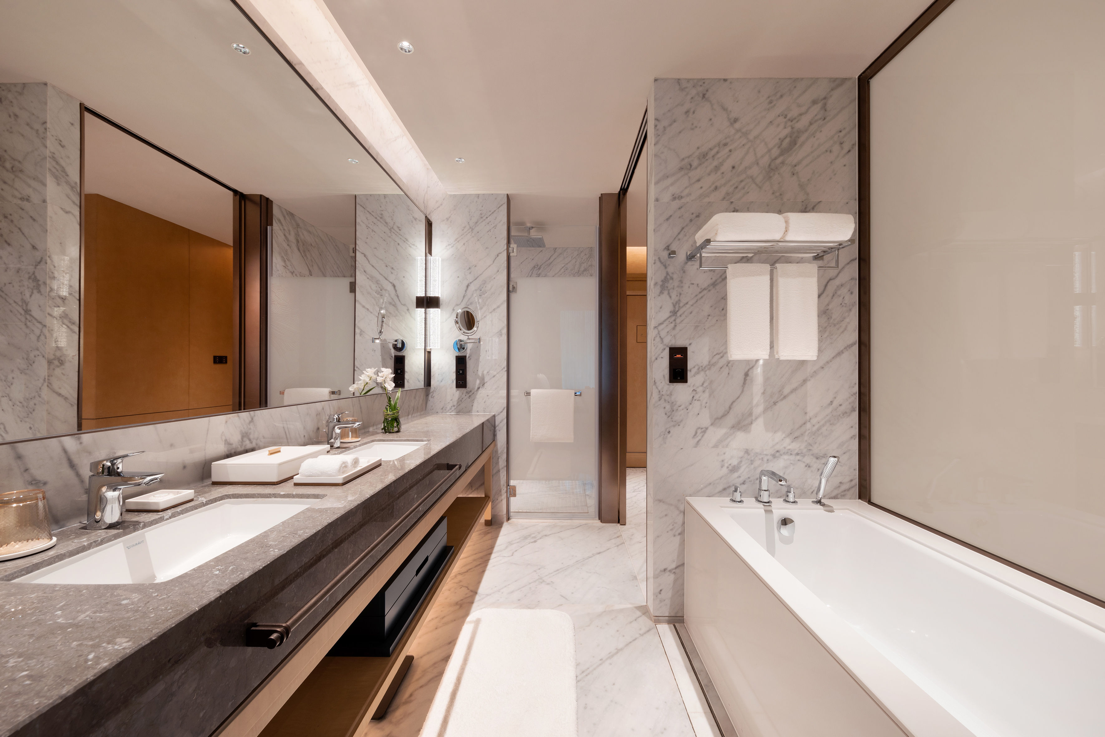 Modern luxury bathroom with marble double vanity, bathtub, and glass shower.