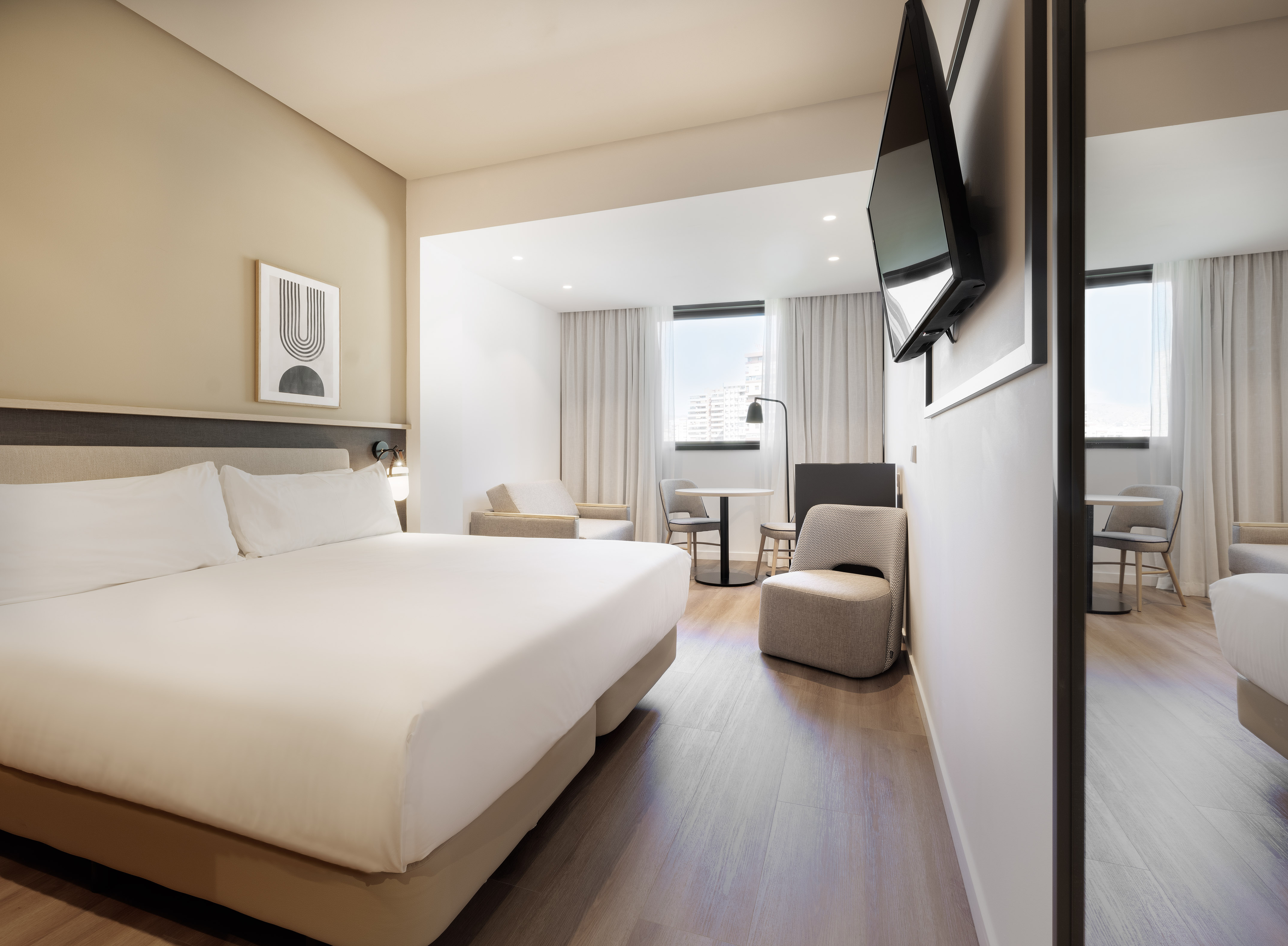 Contemporary hotel suite with king bed, lounge area, and flat-screen TV.