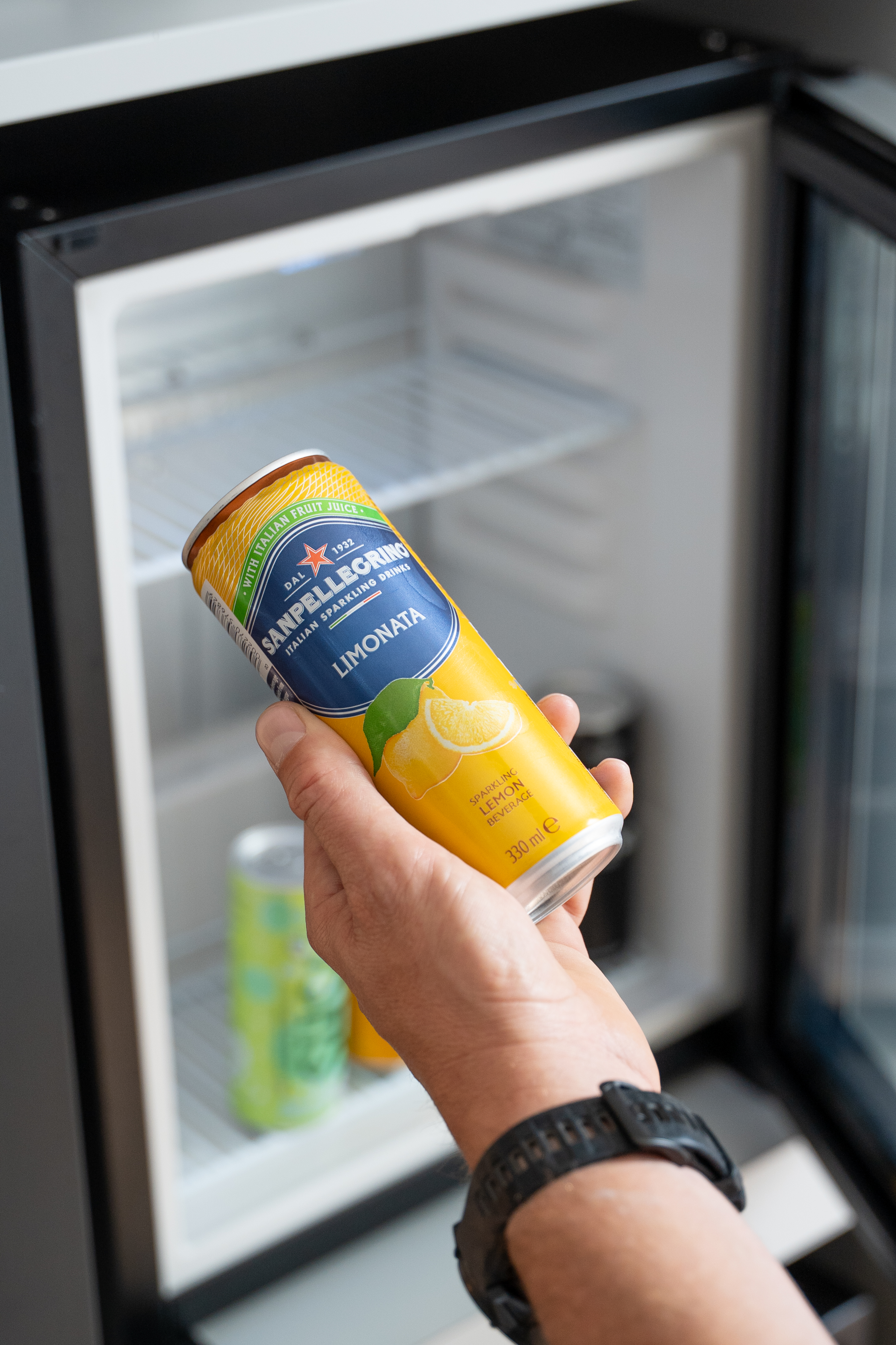 Hand holding Sanpellegrino Limonata sparkling lemon can from a mini-fridge.