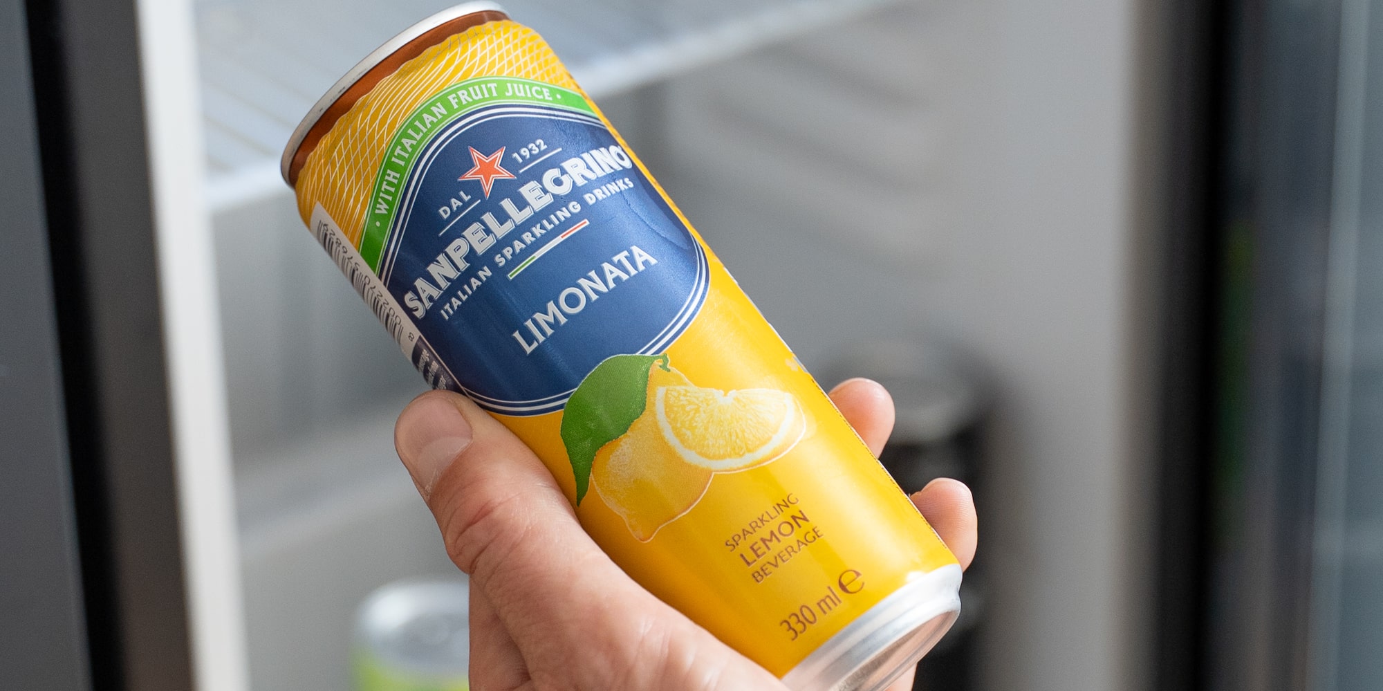 Hand holding Sanpellegrino Limonata sparkling lemon can from a mini-fridge.