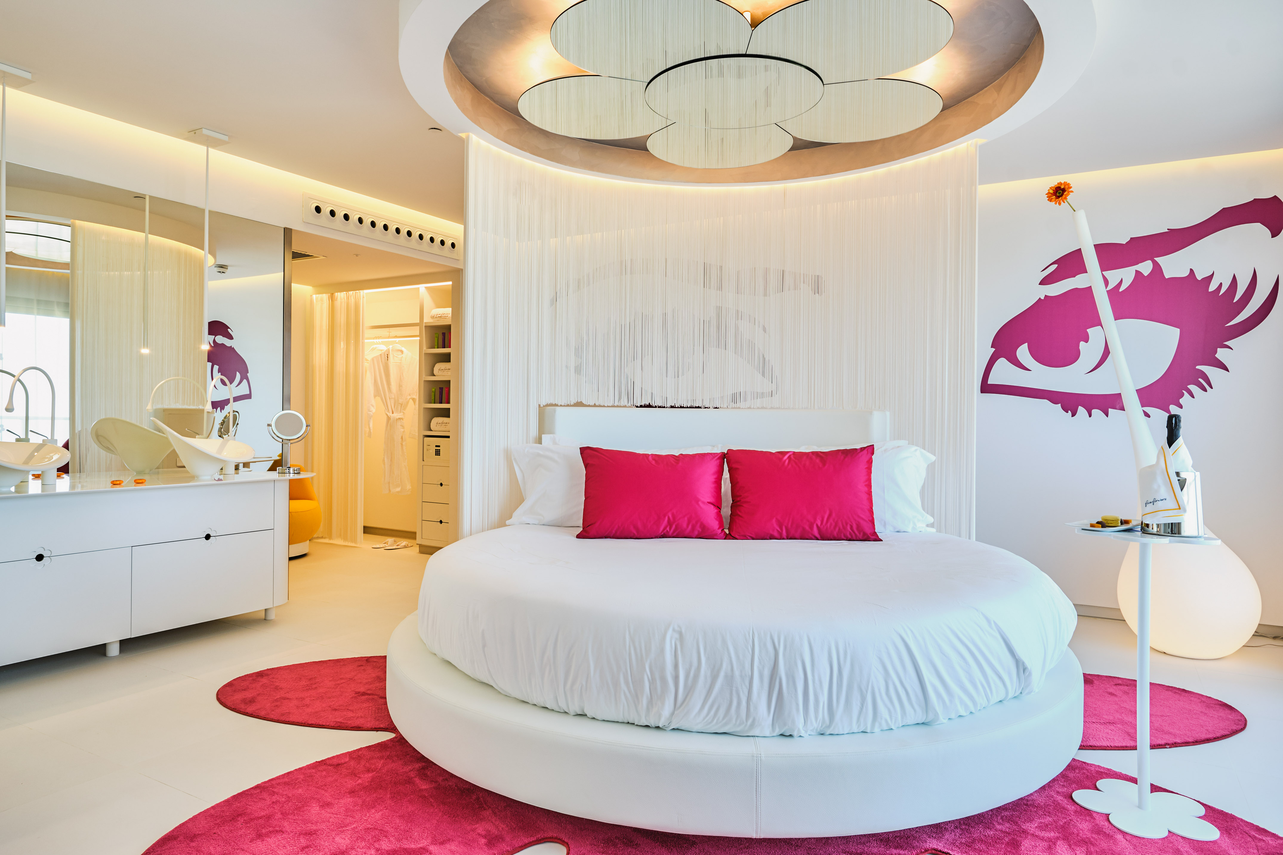 Luxury hotel bedroom with round bed, vibrant pink accents, and modern design.