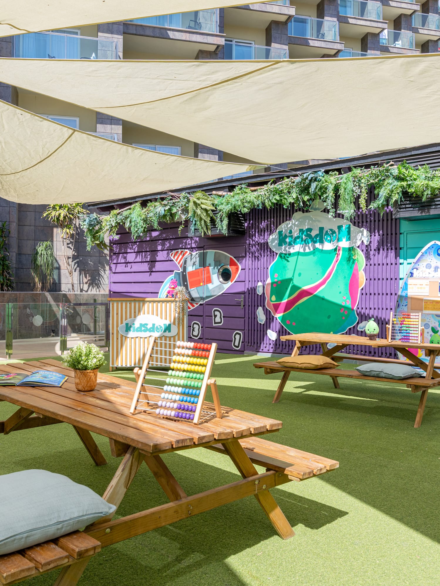 Shaded outdoor kids' club with colorful murals, picnic tables, and green turf.