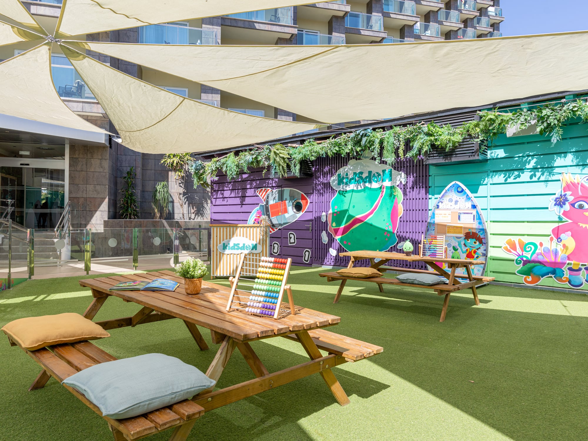 Shaded outdoor kids' club with colorful murals, picnic tables, and green turf.
