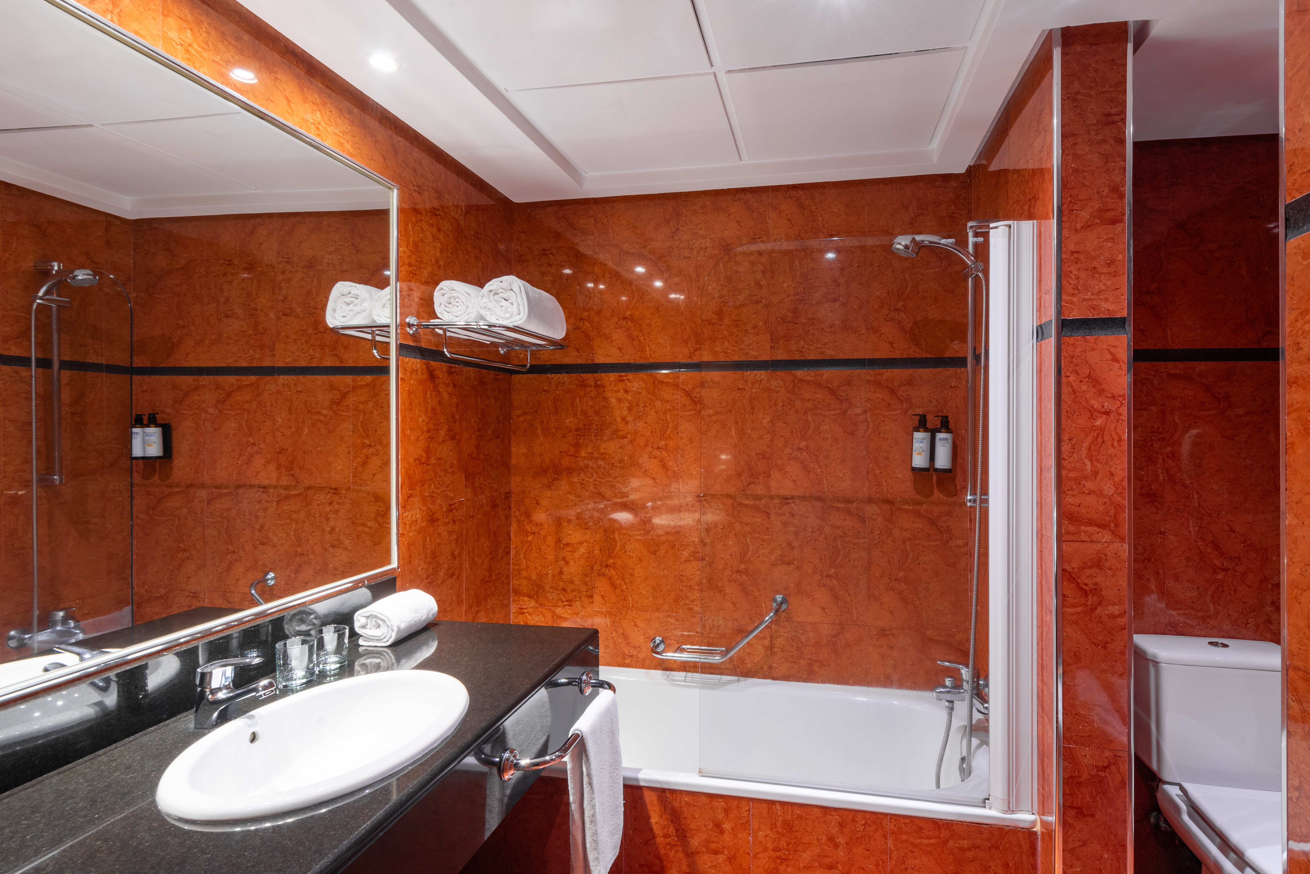 Hotel bathroom with orange tiled walls, black vanity, white sink, and bathtub.