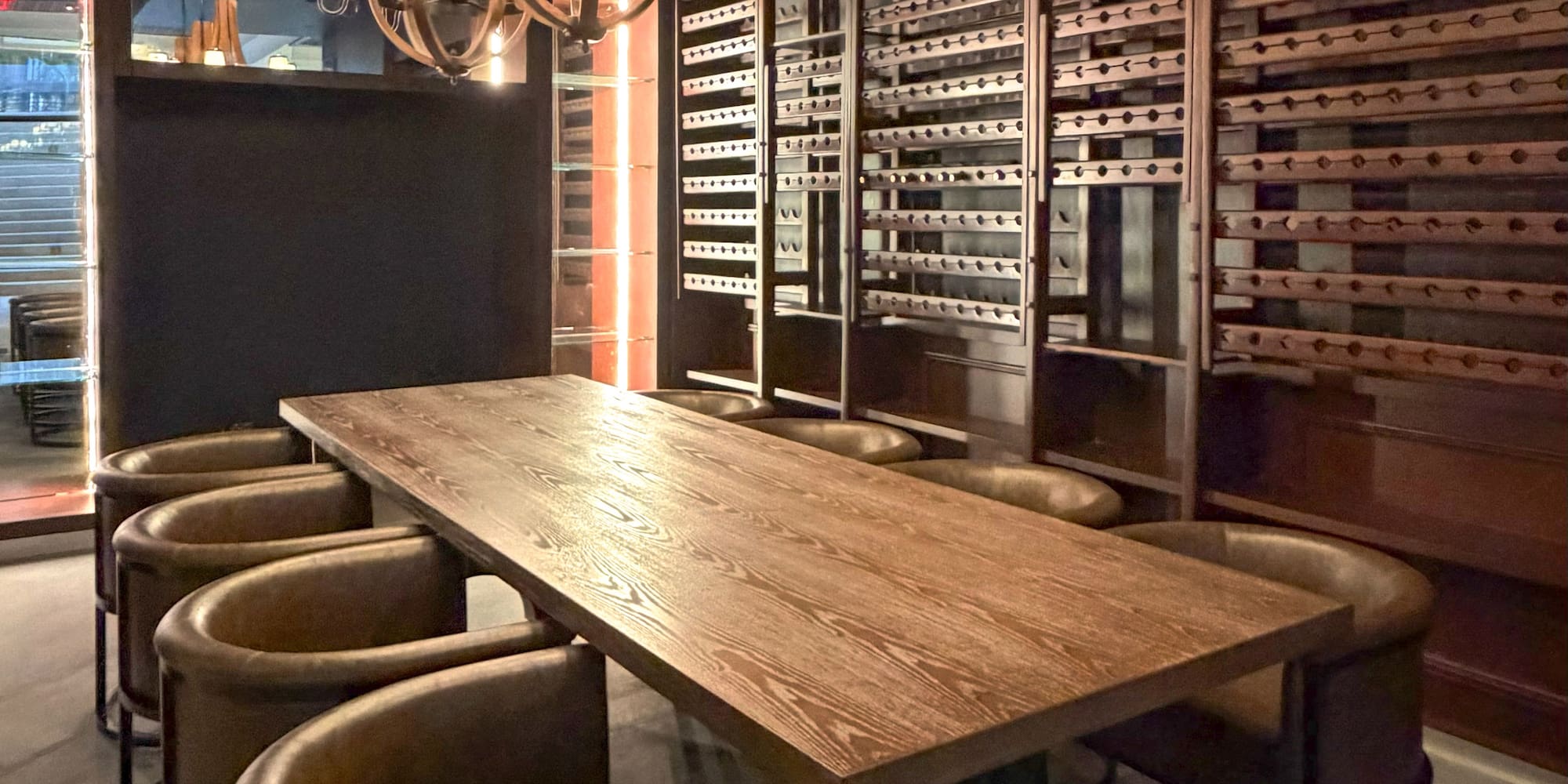 Private wine room with long wooden table, leather chairs, and chandeliers.