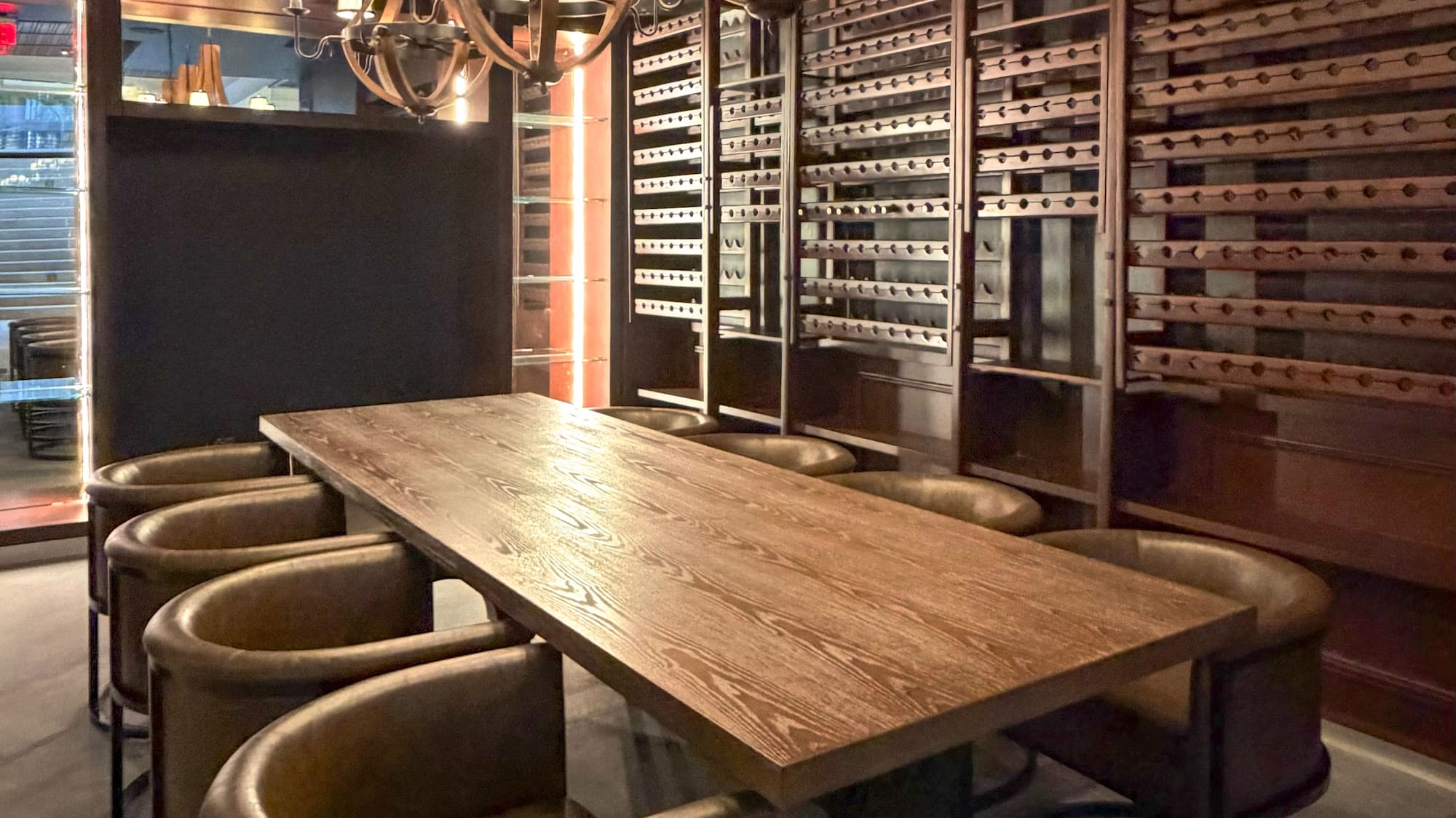 Private wine room with long wooden table, leather chairs, and chandeliers.