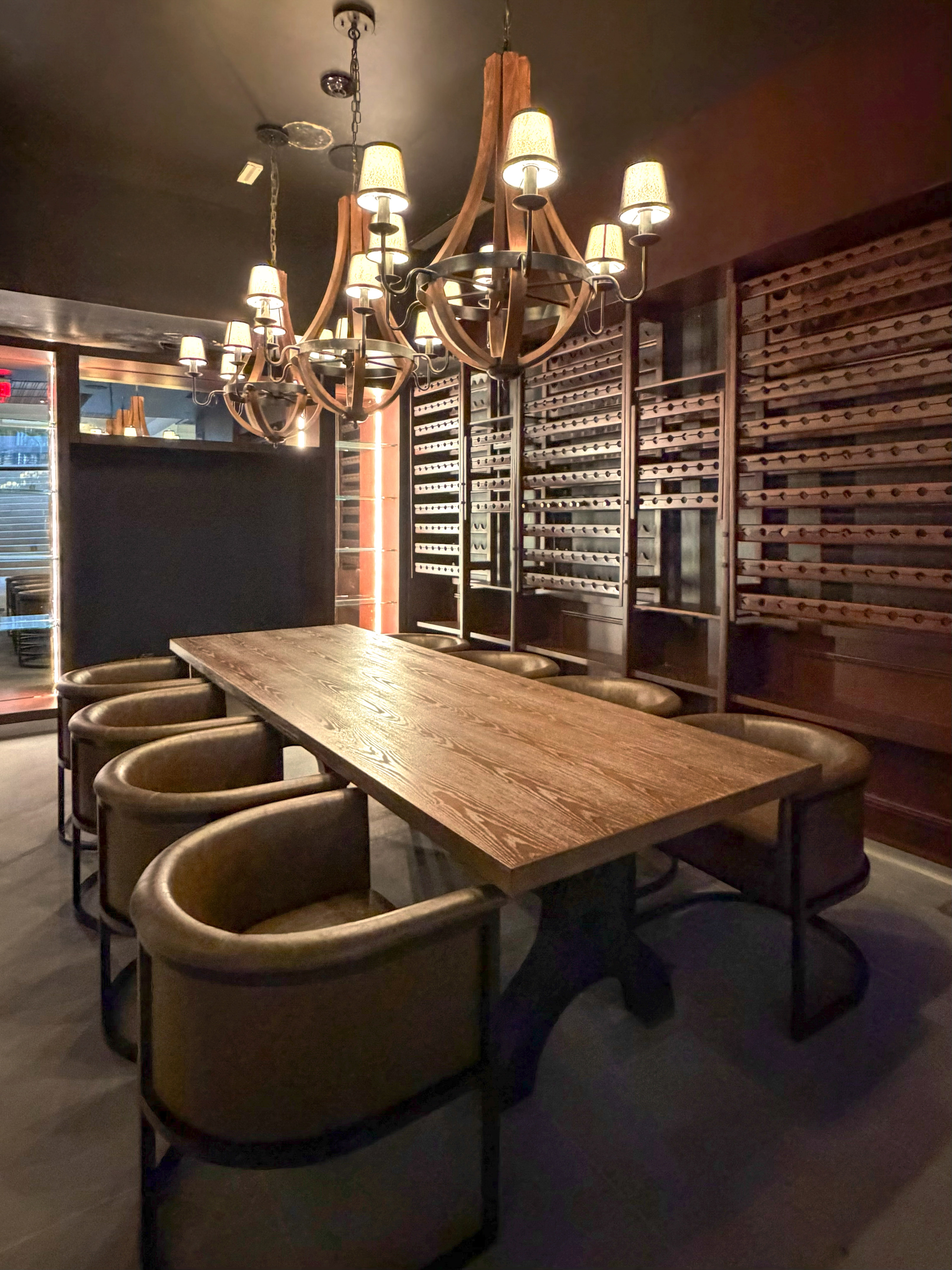 Private wine room with long wooden table, leather chairs, and chandeliers.