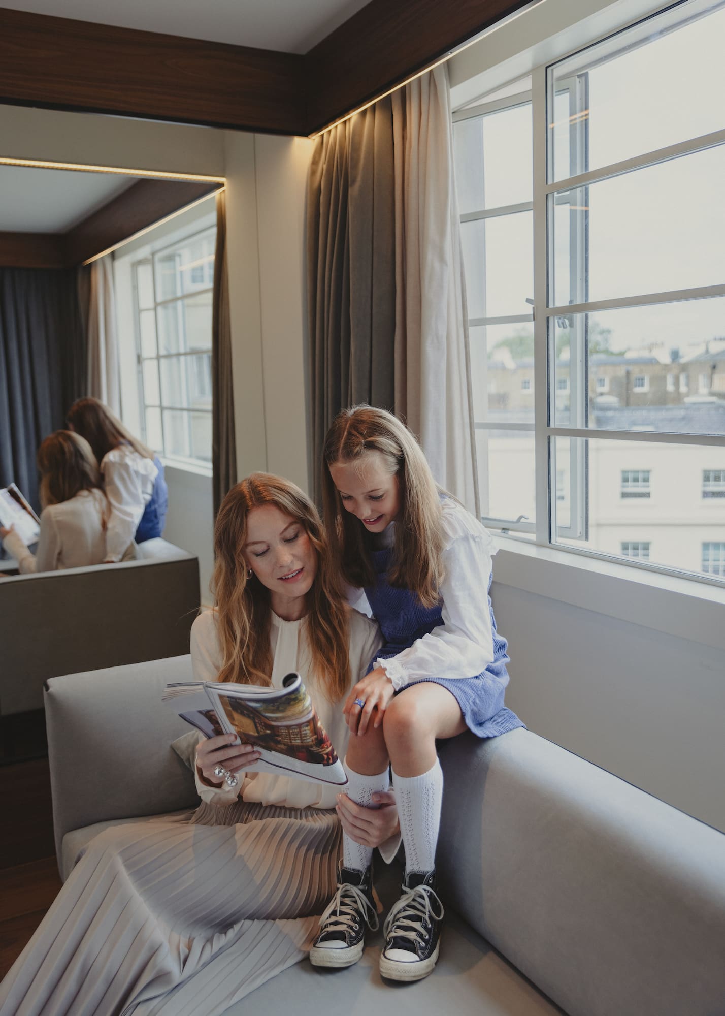 a woman and a girl sitting on a couch reading a magazine