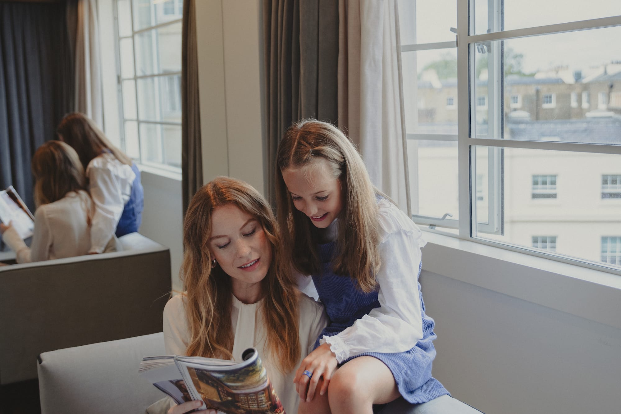 a woman and a girl sitting on a couch reading a magazine