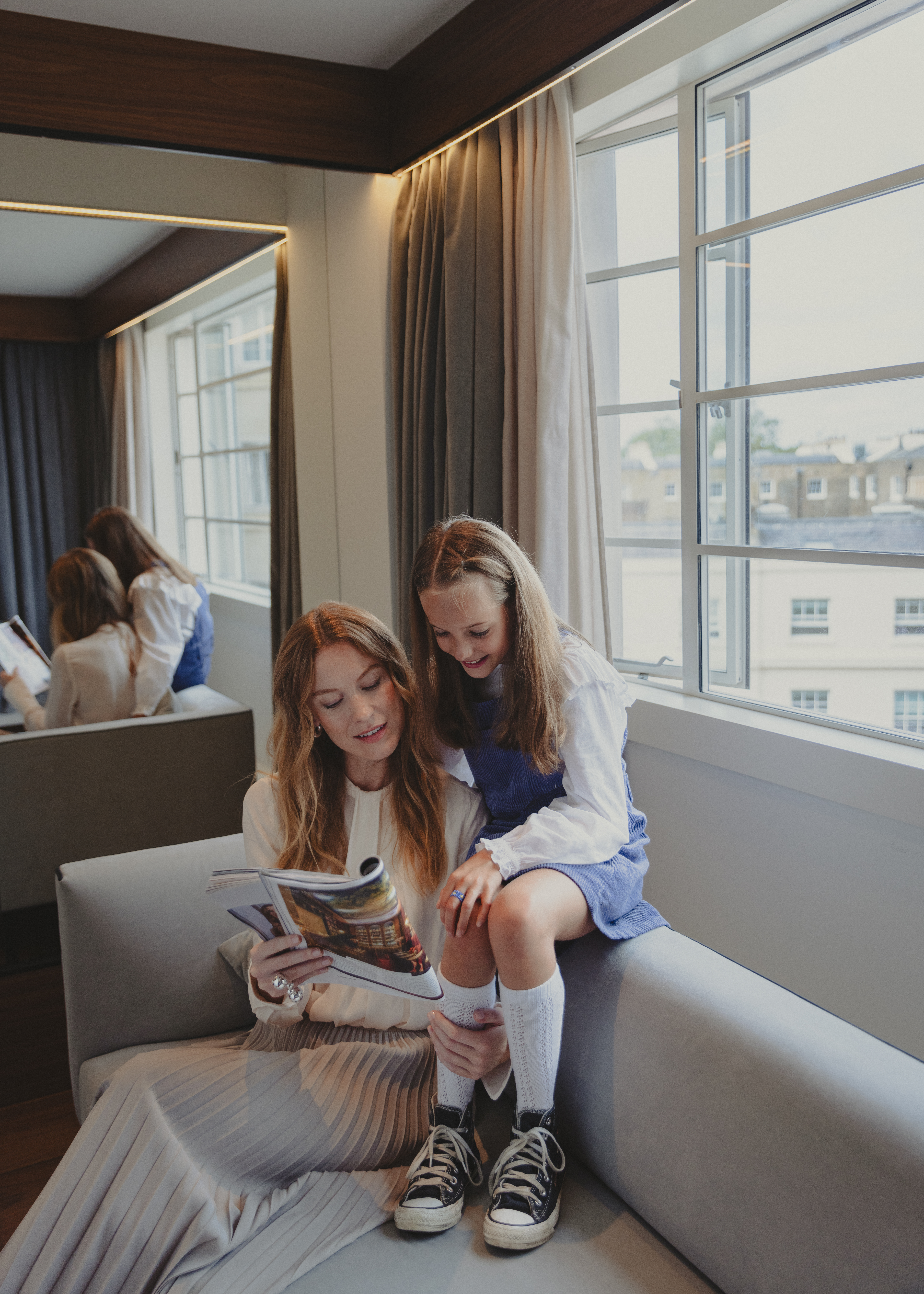 a woman and a girl sitting on a couch reading a magazine