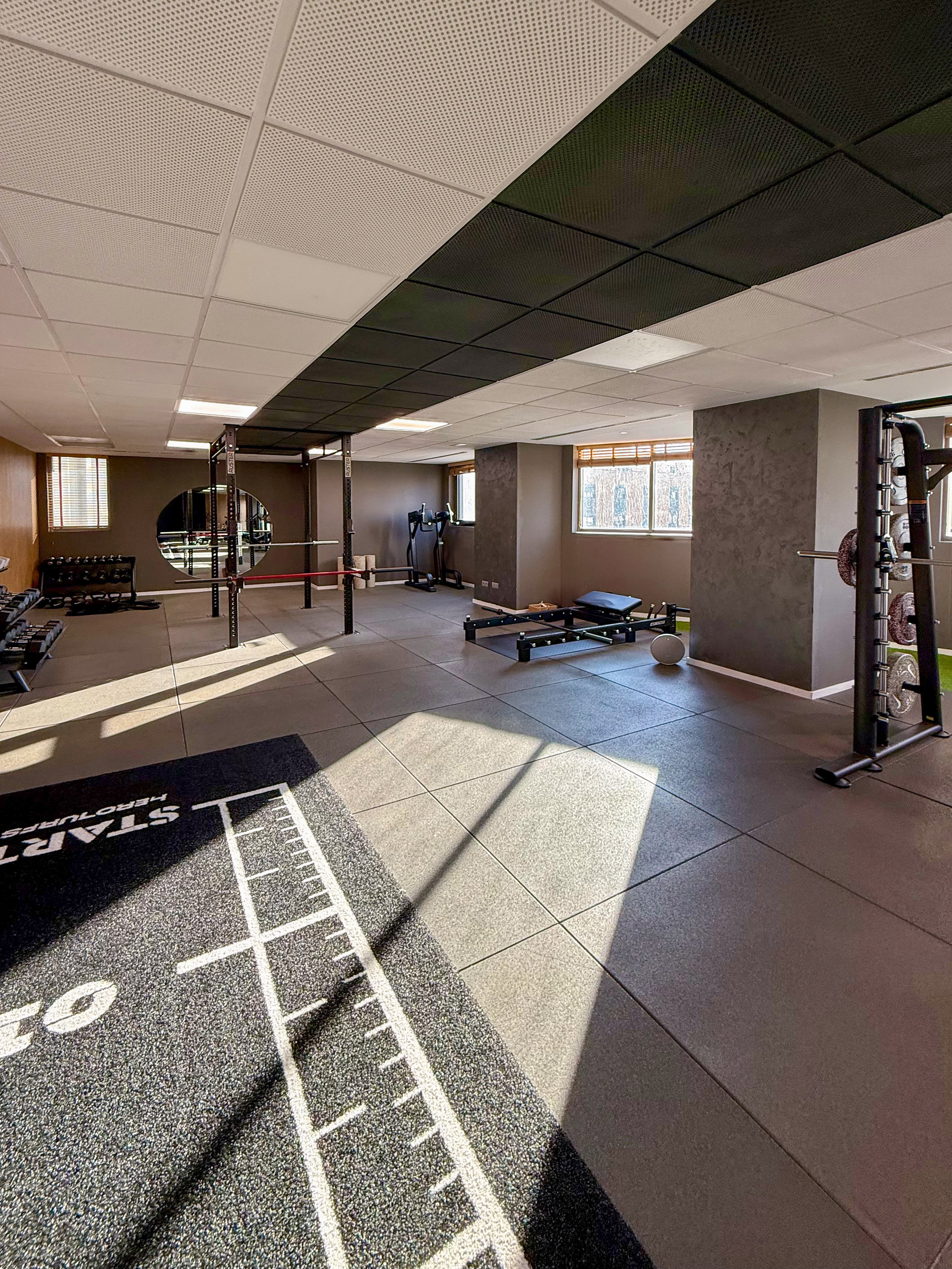 Modern gym interior with workout equipment, rubber floor, and sunny windows.