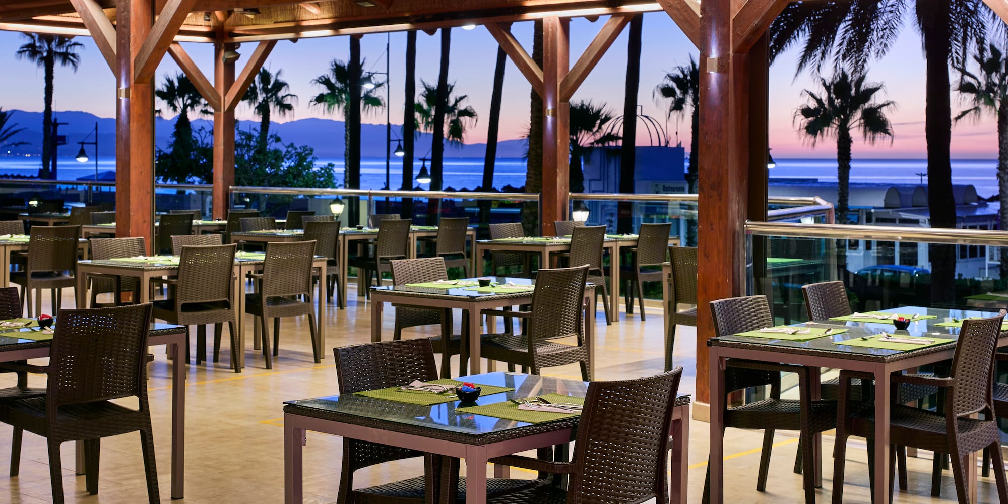 Outdoor resort restaurant with sea view, palm trees at sunset.
