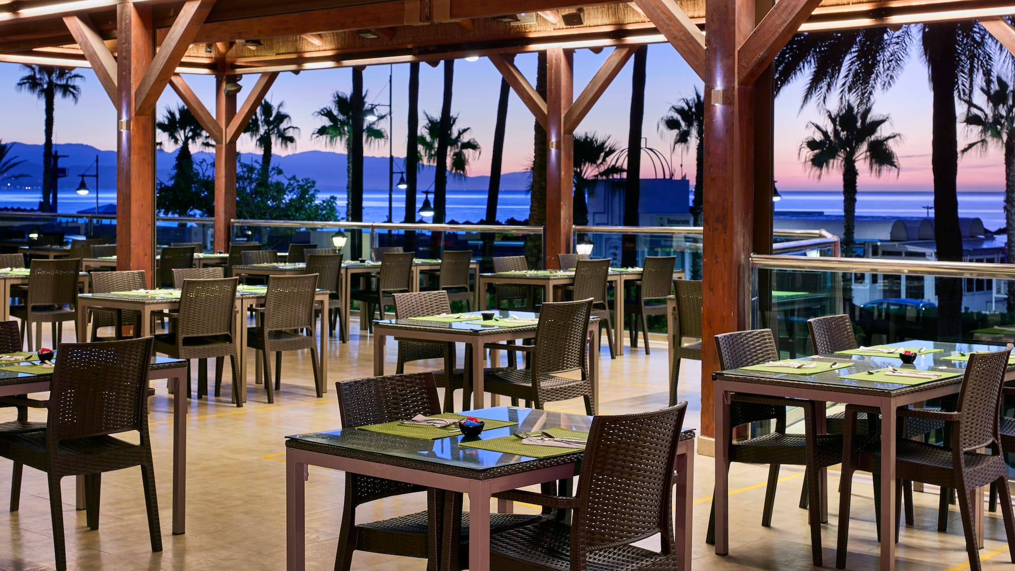 Outdoor resort restaurant with sea view, palm trees at sunset.