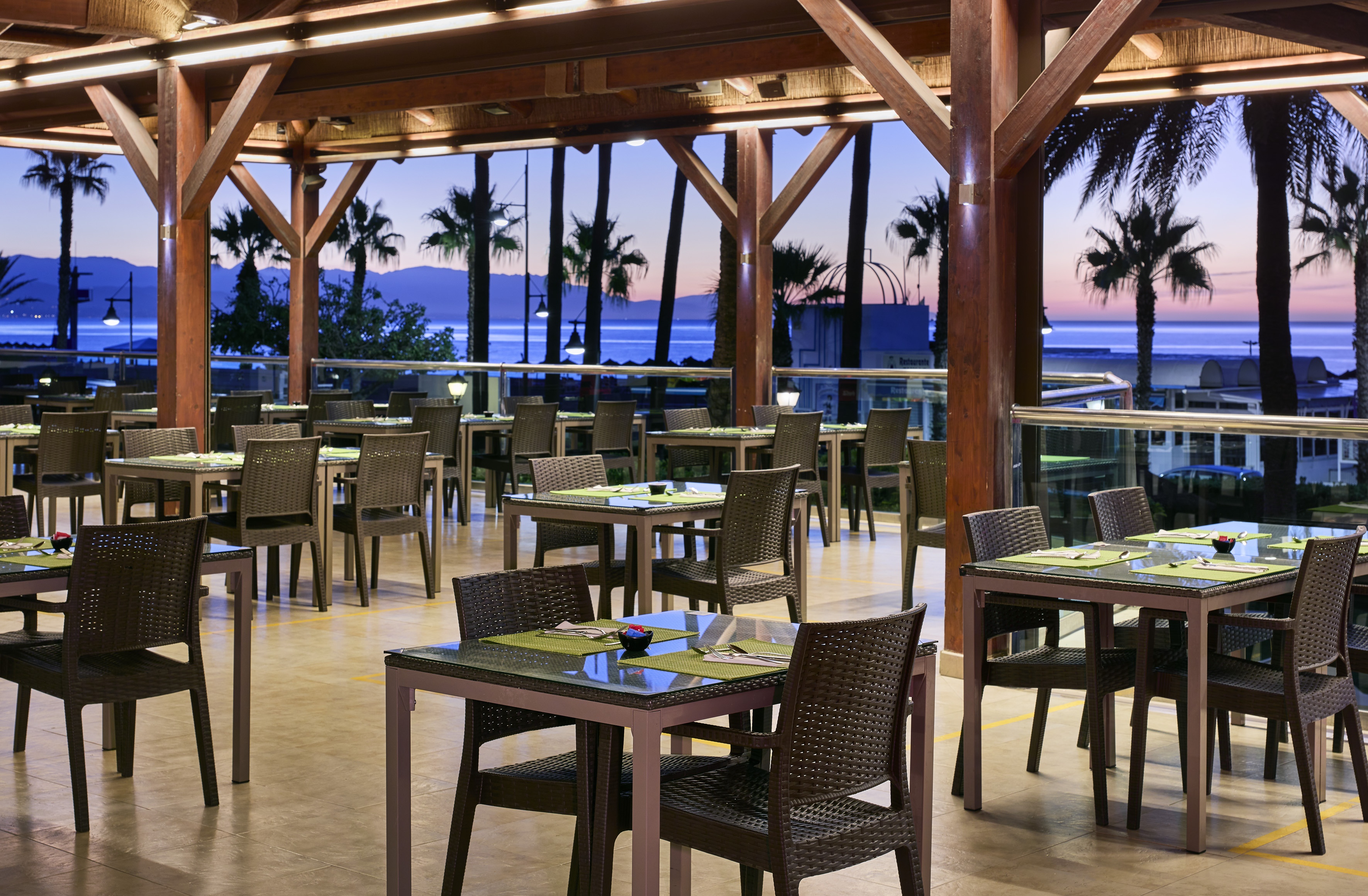 Outdoor resort restaurant with sea view, palm trees at sunset.