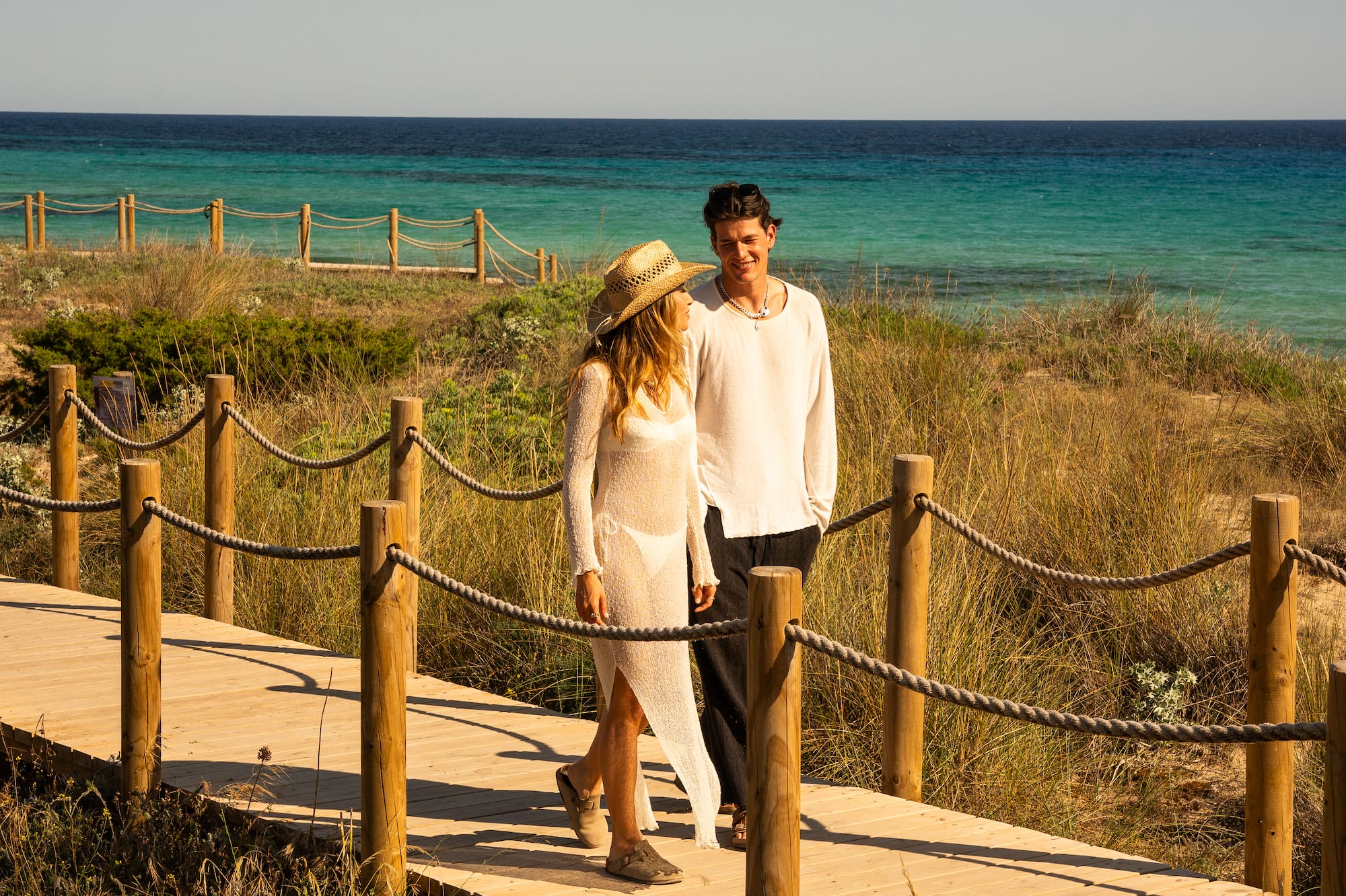 a man and woman walking on a wooden walkway by the water