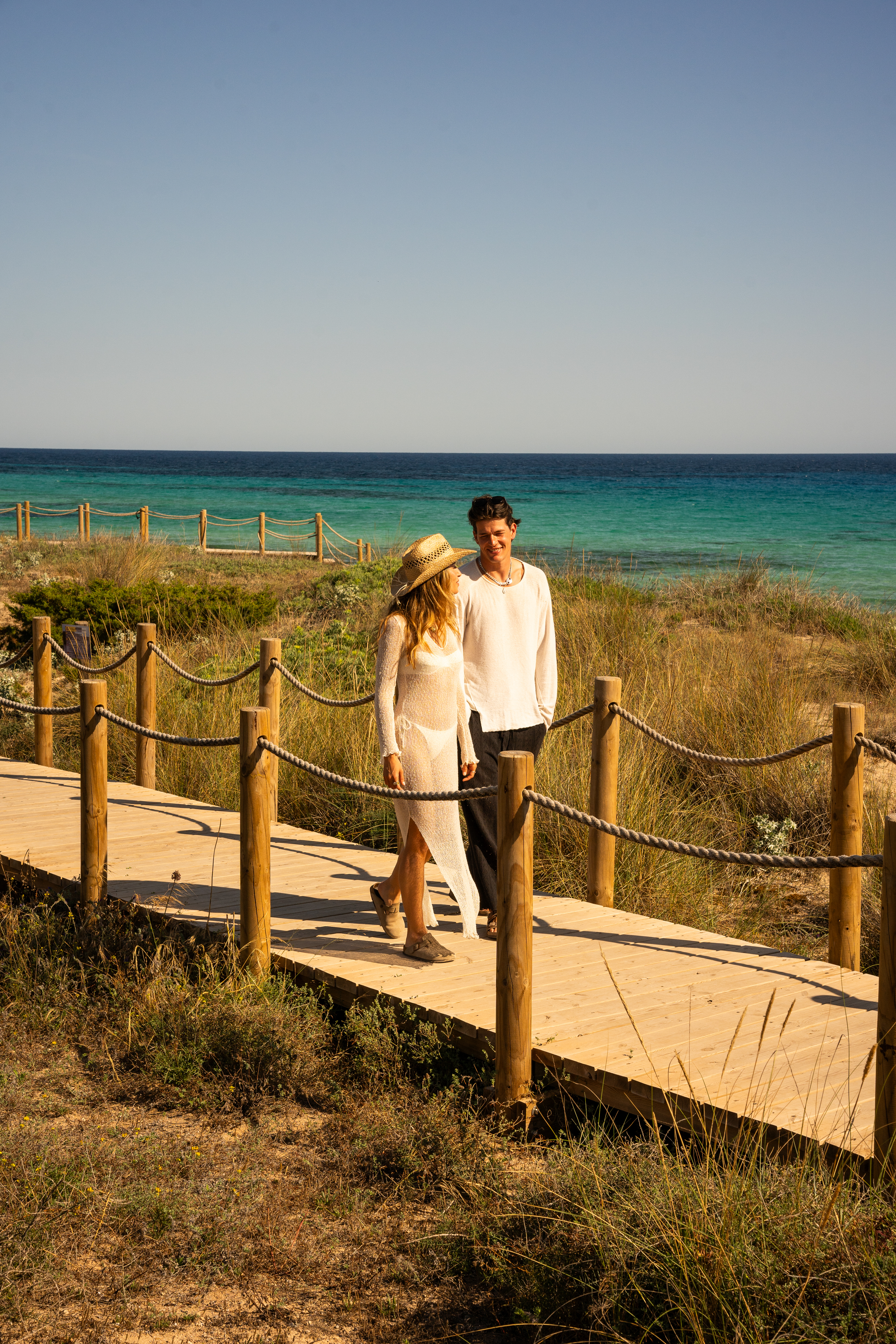 a man and woman walking on a wooden walkway by the water