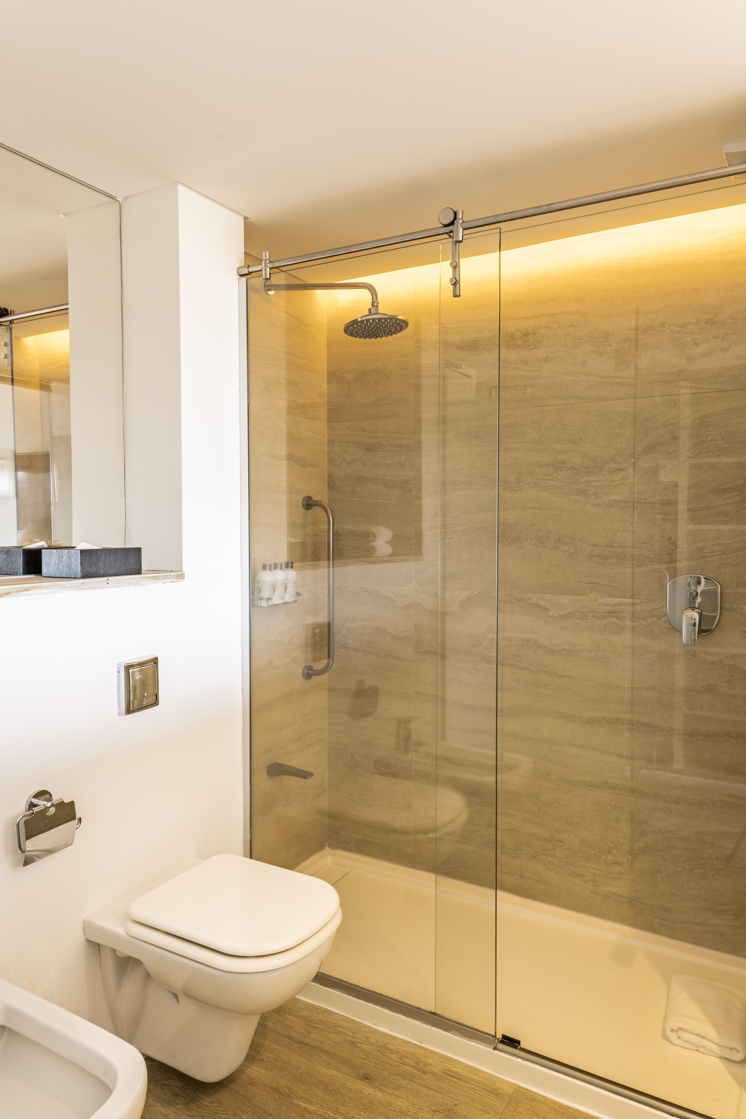 Modern bathroom with walk-in glass shower, rain shower, toilet, and bidet.