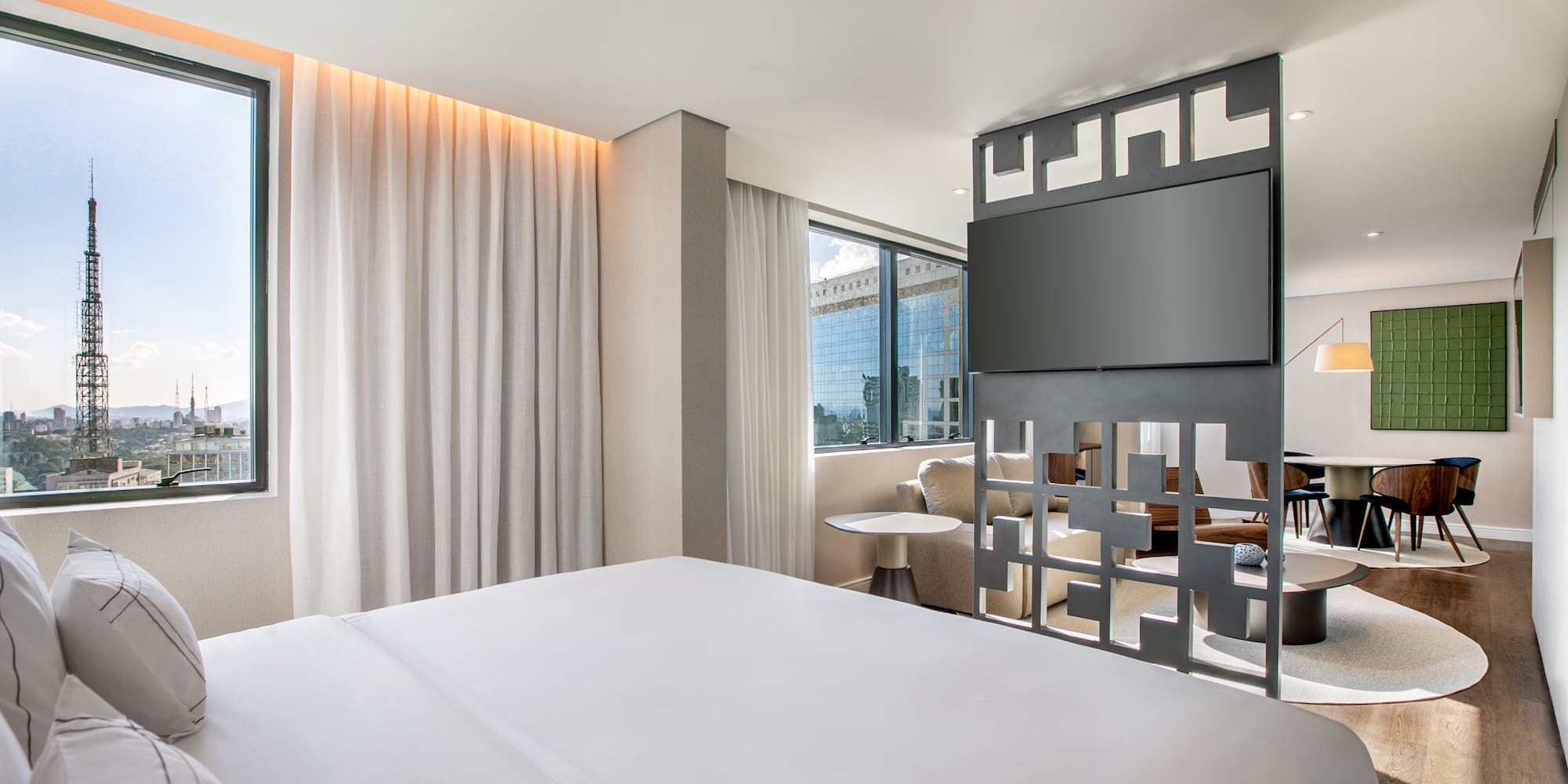 Modern hotel suite: bedroom with city view, TV, and adjoining living area.