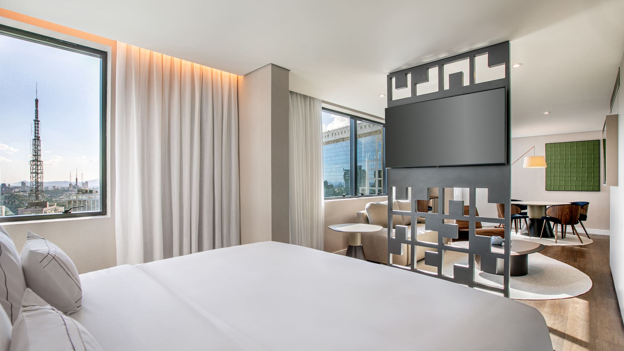 Modern hotel suite: bedroom with city view, TV, and adjoining living area.