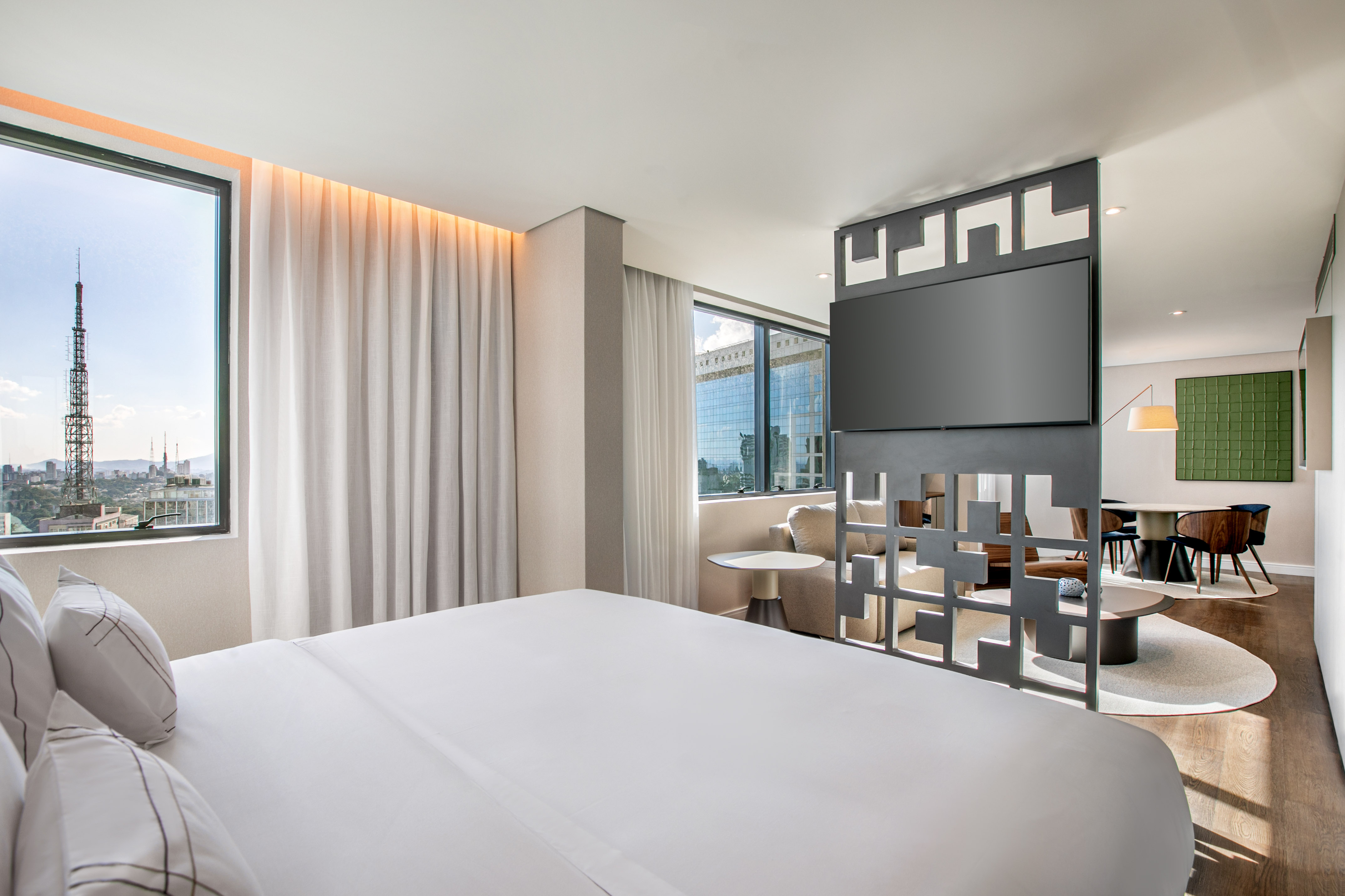 Modern hotel suite: bedroom with city view, TV, and adjoining living area.