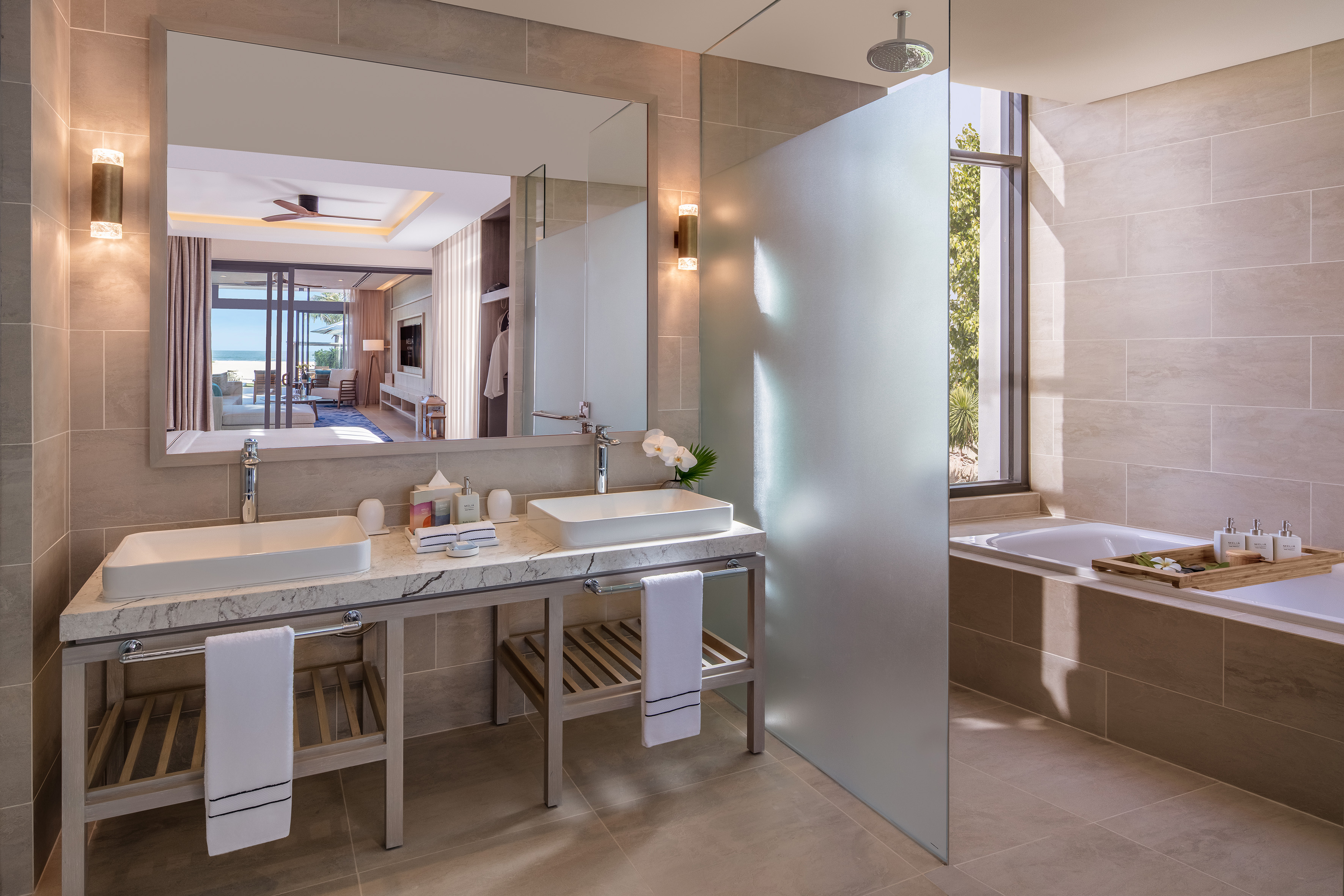 Luxury bathroom, double vanity, shower, tub, mirror reflects ocean view.