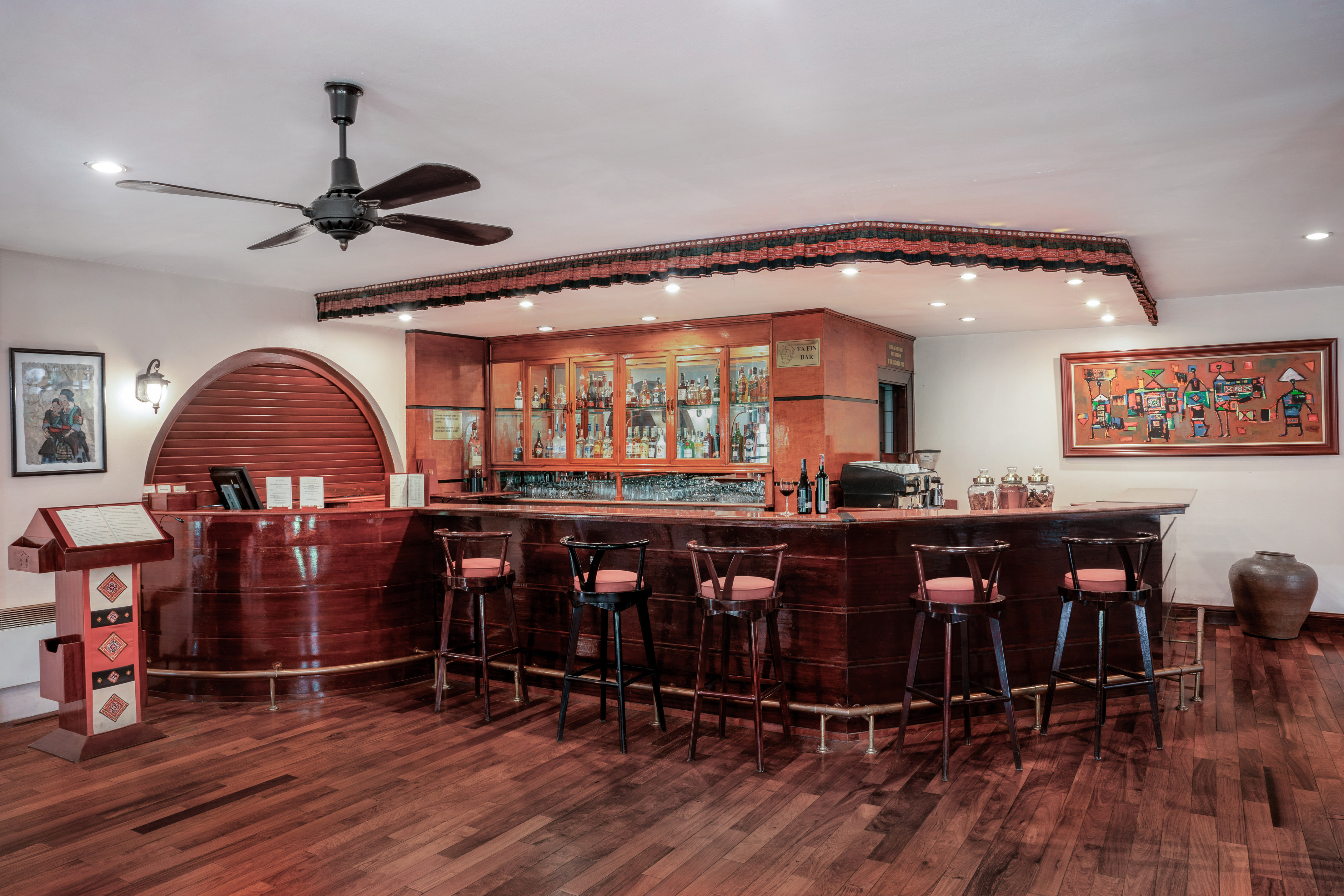 Stylish wooden hotel bar with liquor display, bar stools, and hardwood floor.