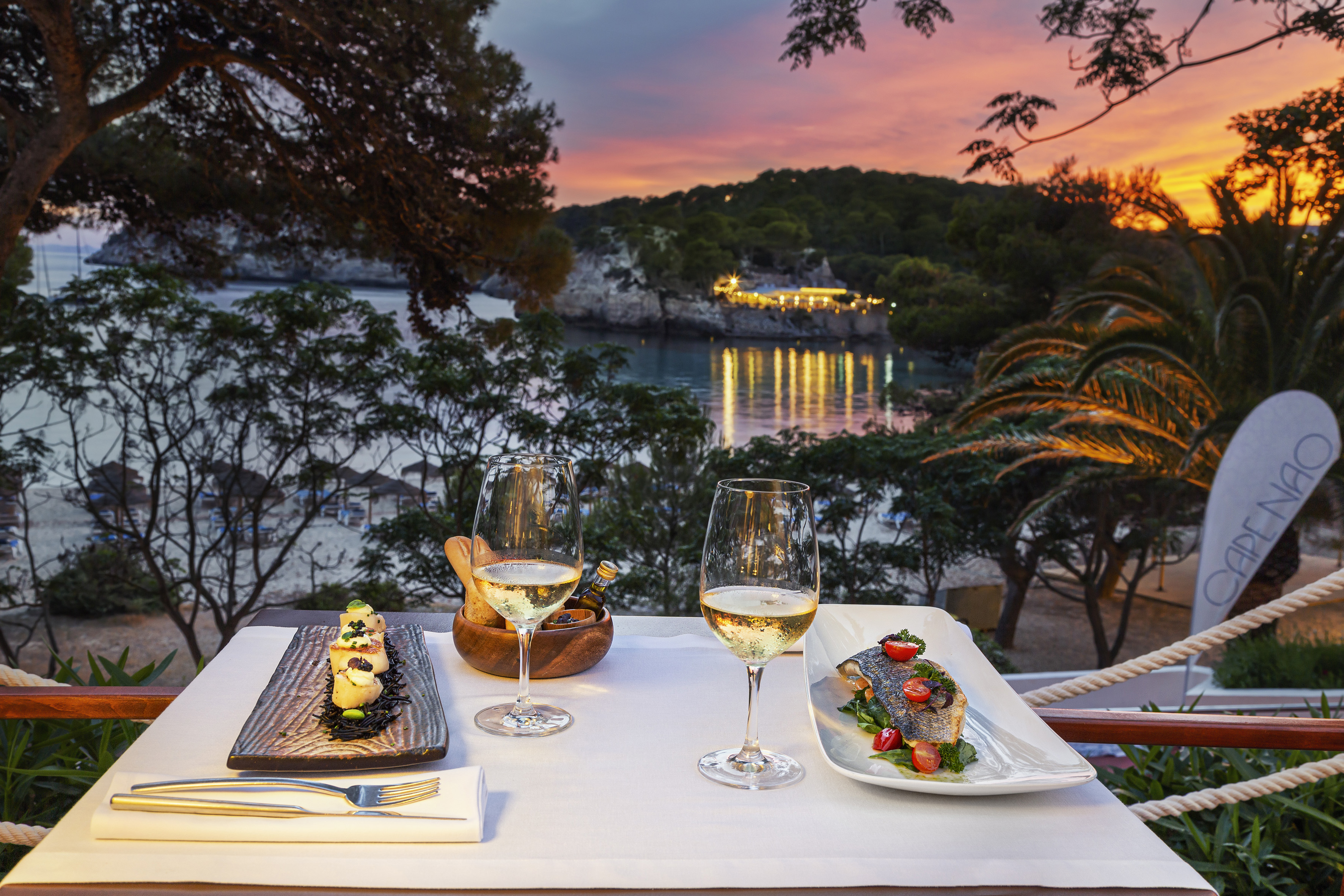 Fine dining at sunset: seafood, wine, and a coastal bay view.