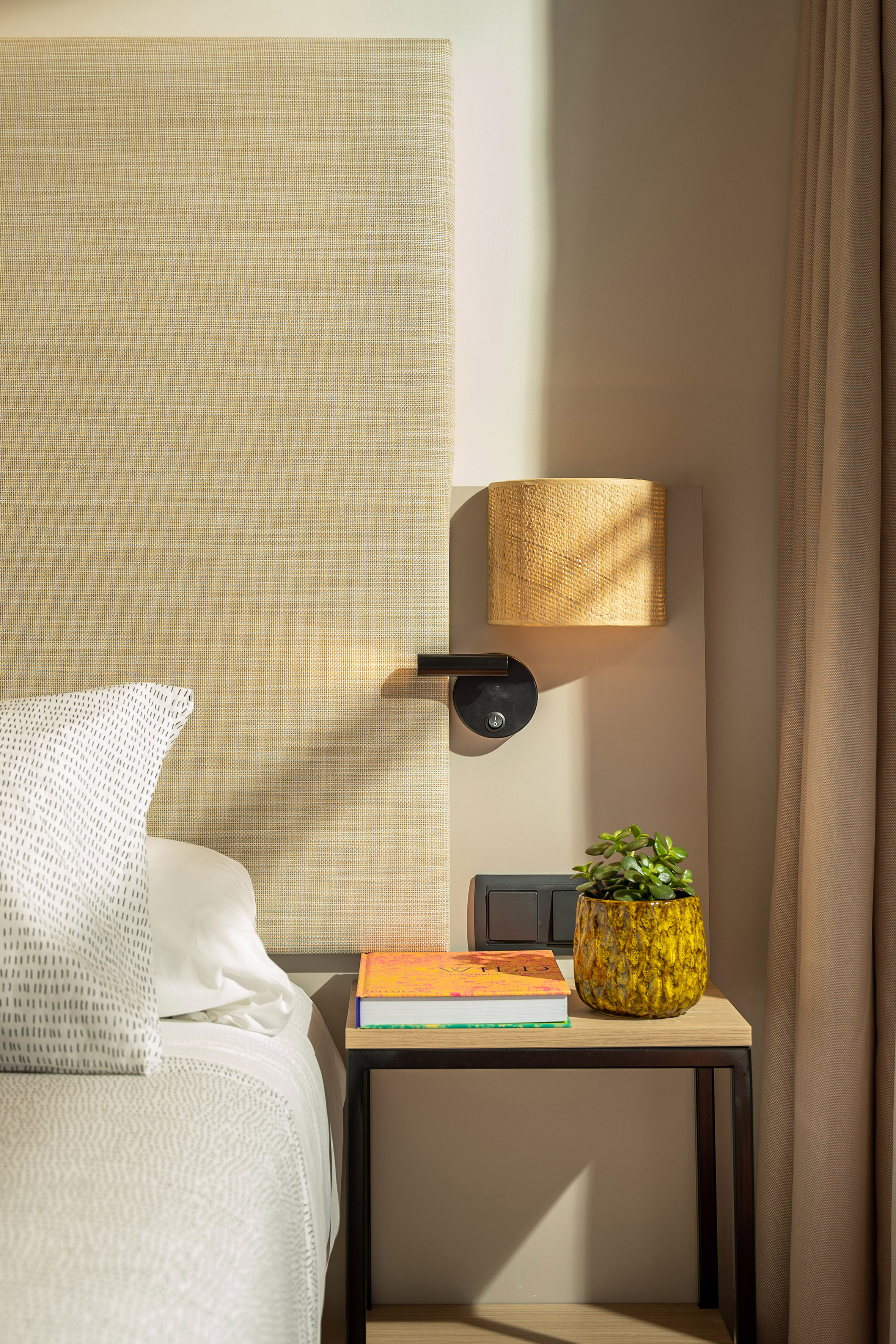 Bedroom nightstand with woven lamp, succulent, book, and cozy bedding.
