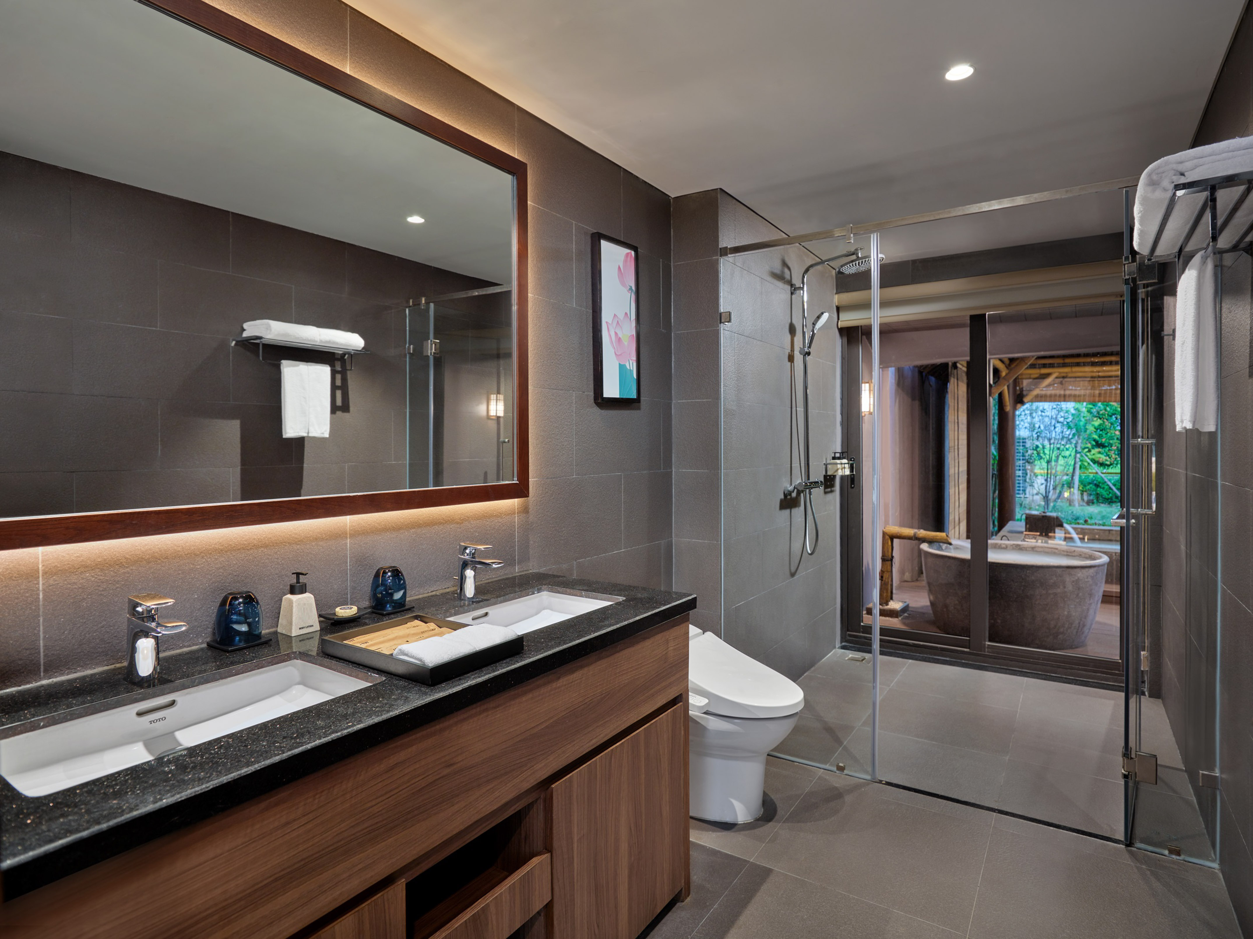 Luxury hotel bathroom: double vanity, glass shower, outdoor stone tub view.