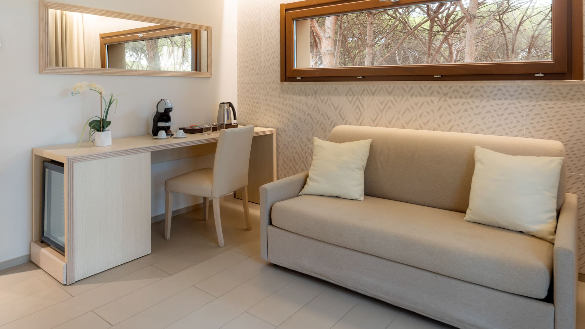 Modern hotel room with sofa, desk, coffee station, and nature view window.
