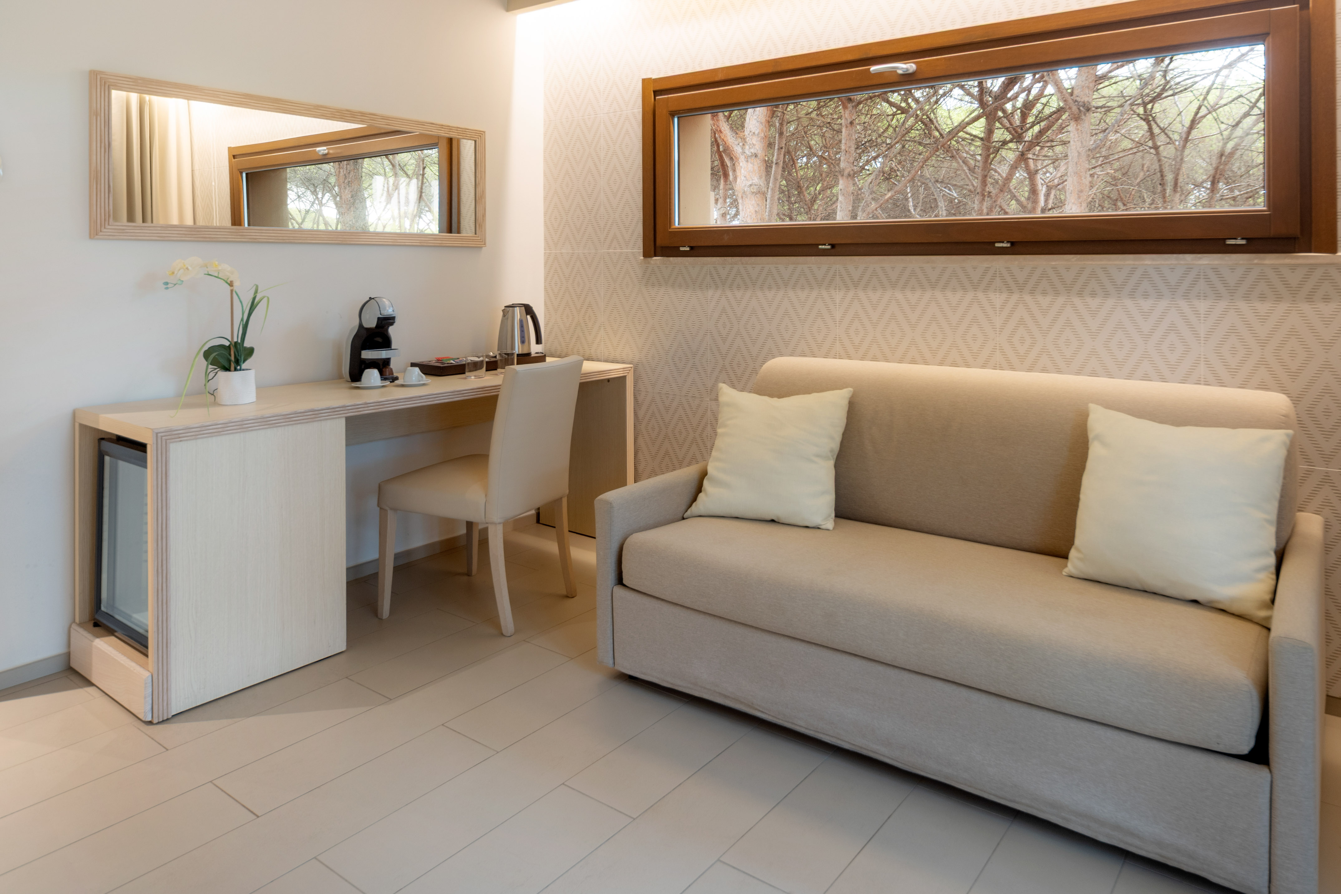 Modern hotel room with sofa, desk, coffee station, and nature view window.