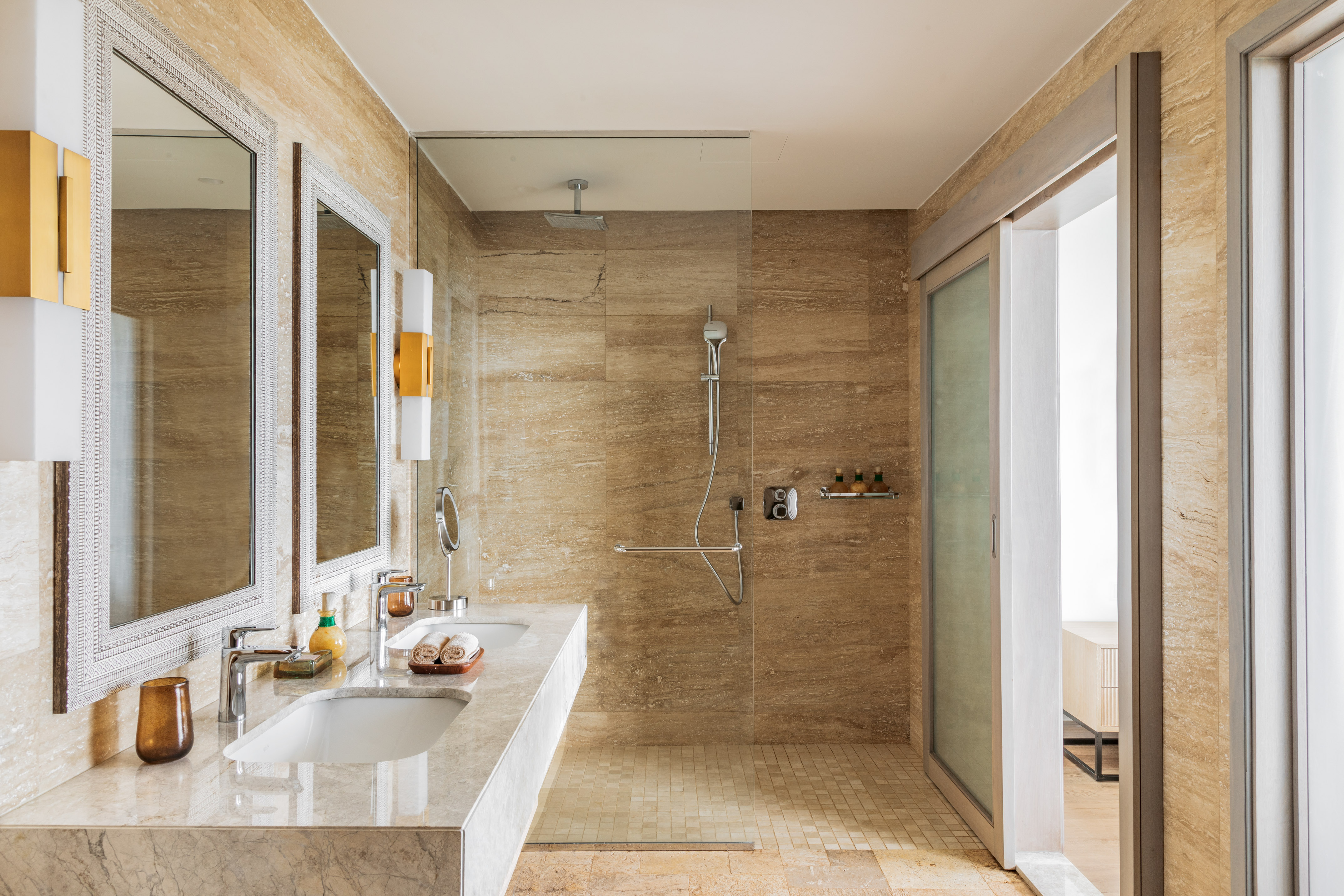 Beige marble bathroom with double vanity, framed mirrors, and glass walk-in shower.