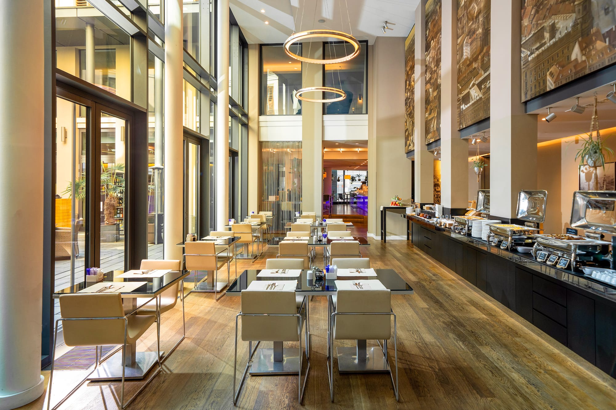 Modern hotel restaurant with a buffet line, set dining tables, and large windows.
