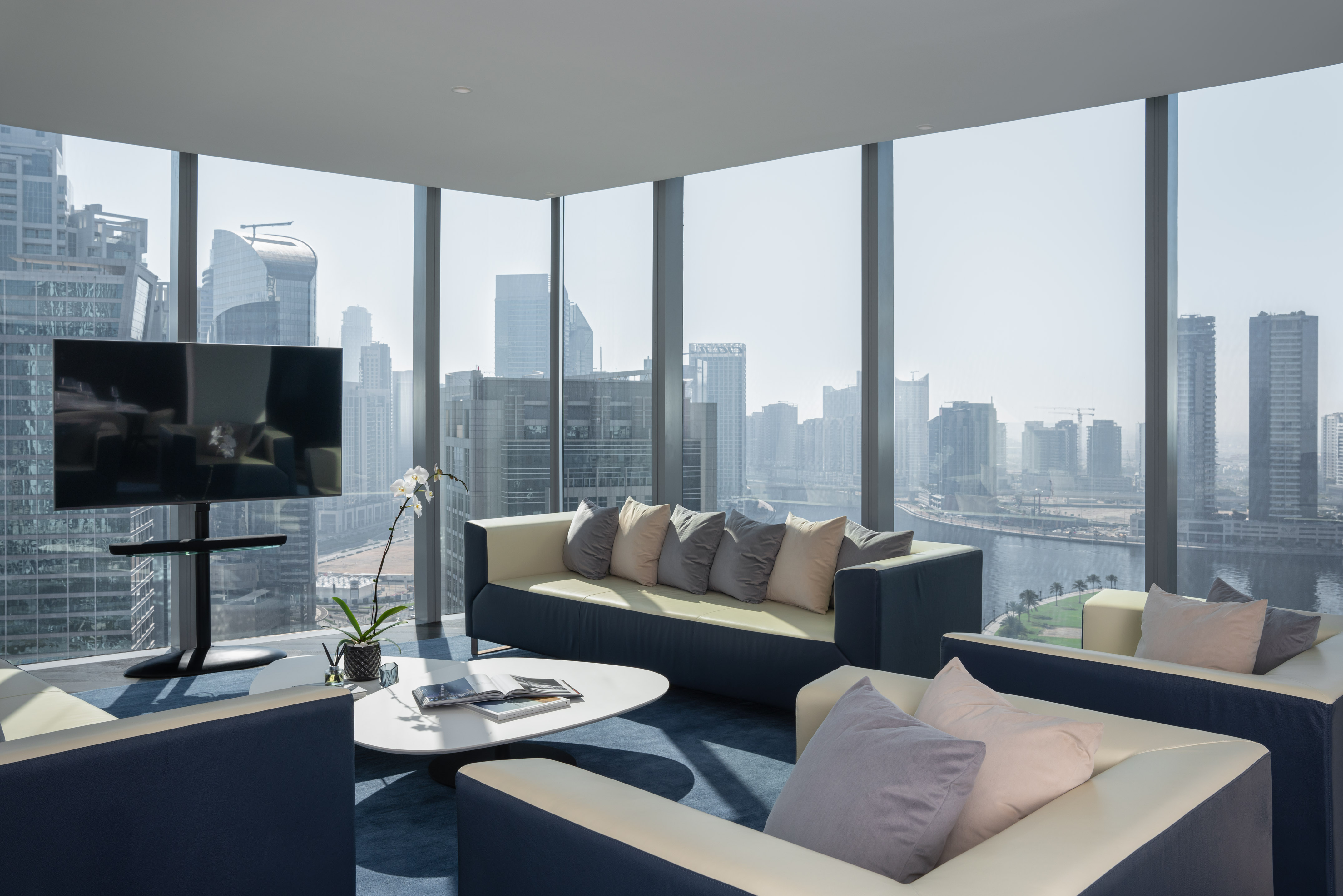 Modern lounge with panoramic city skyline view, blue sofas, and TV. - 2 Bedroom Opus Residence - ME Dubai Residences, دبي