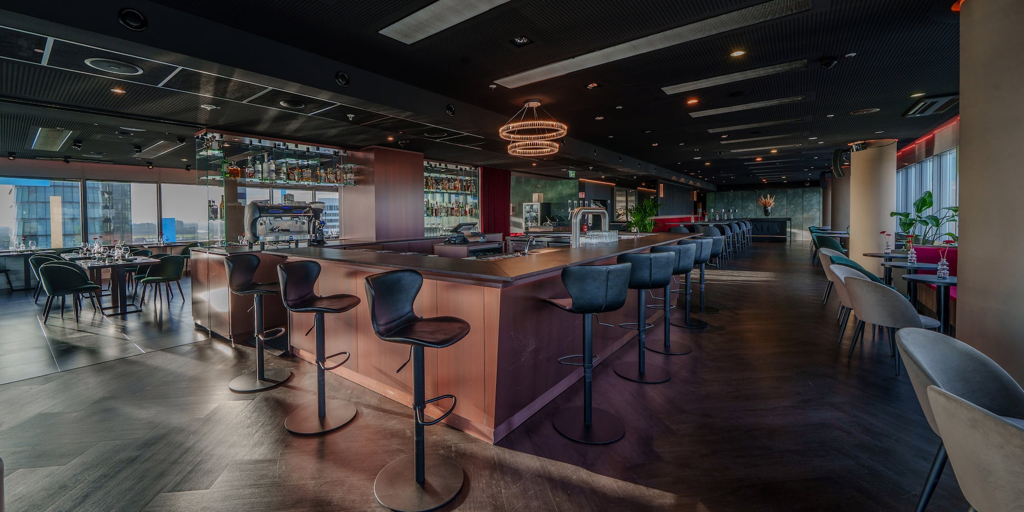 Rooftop bar lounge with dark wood counter, sleek stools, and cityscape view.