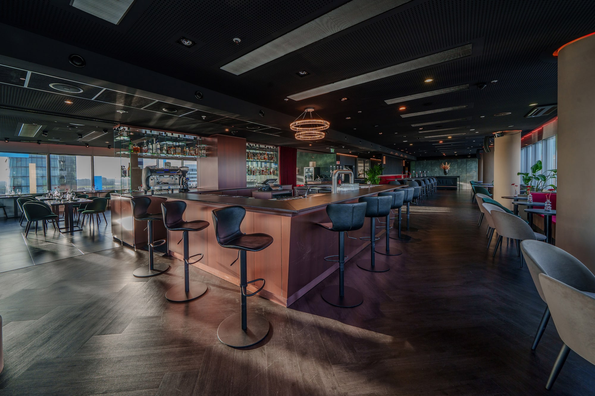 Upscale modern bar interior with wooden counter, black stools, and city view.