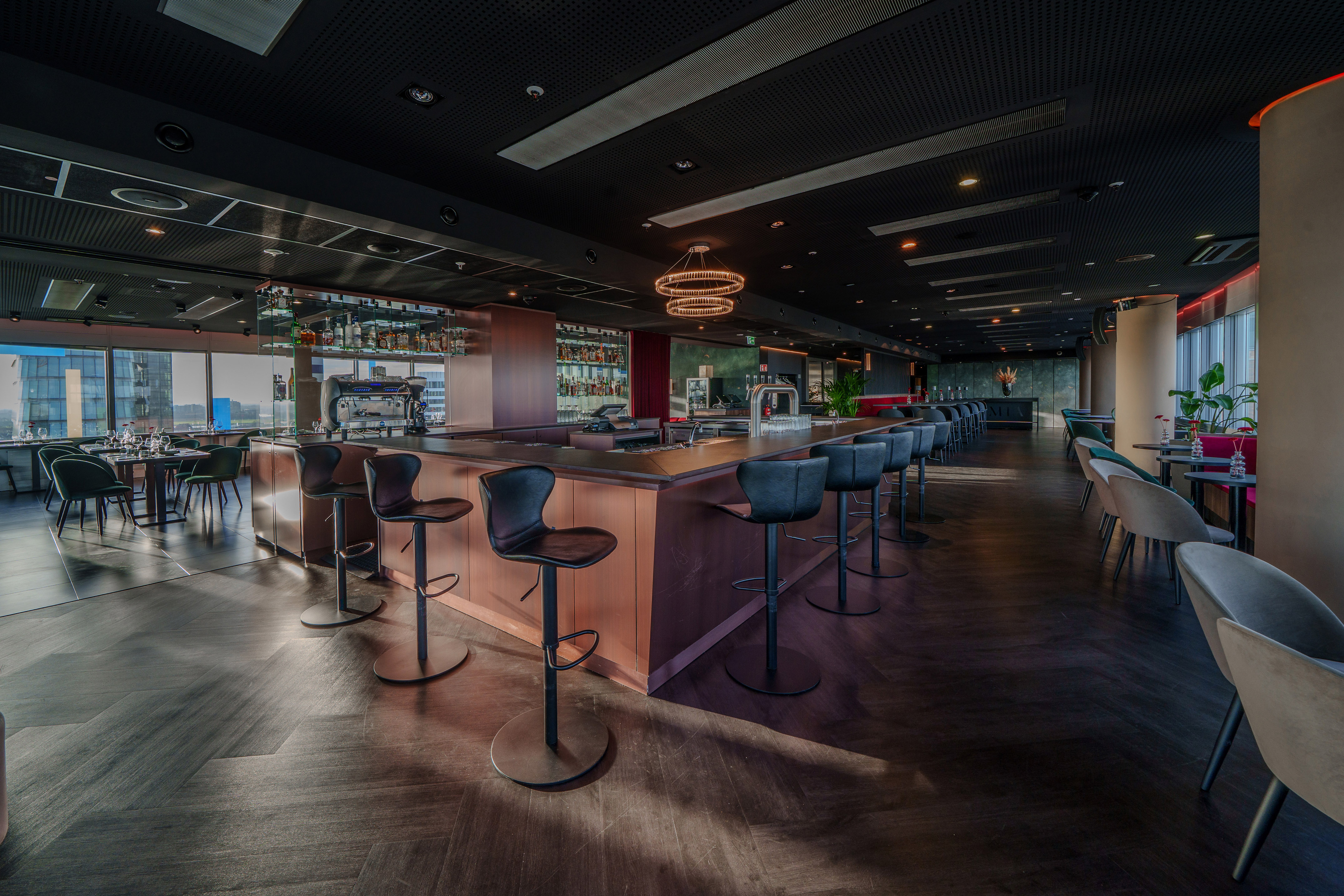 Rooftop bar lounge with dark wood counter, sleek stools, and cityscape view.
