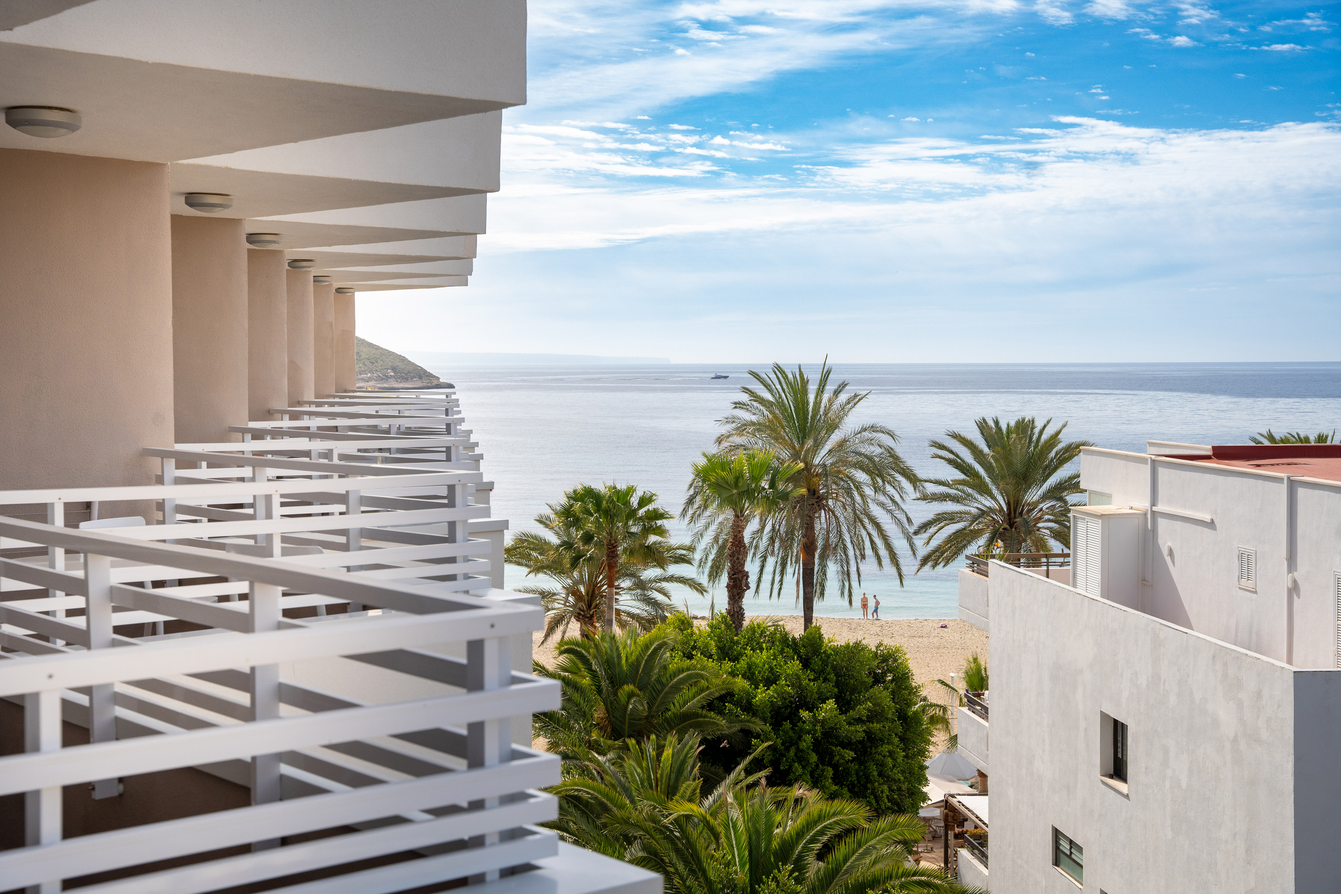 Resort balcony overlooking beach, palm trees, and blue Mediterranean sea.