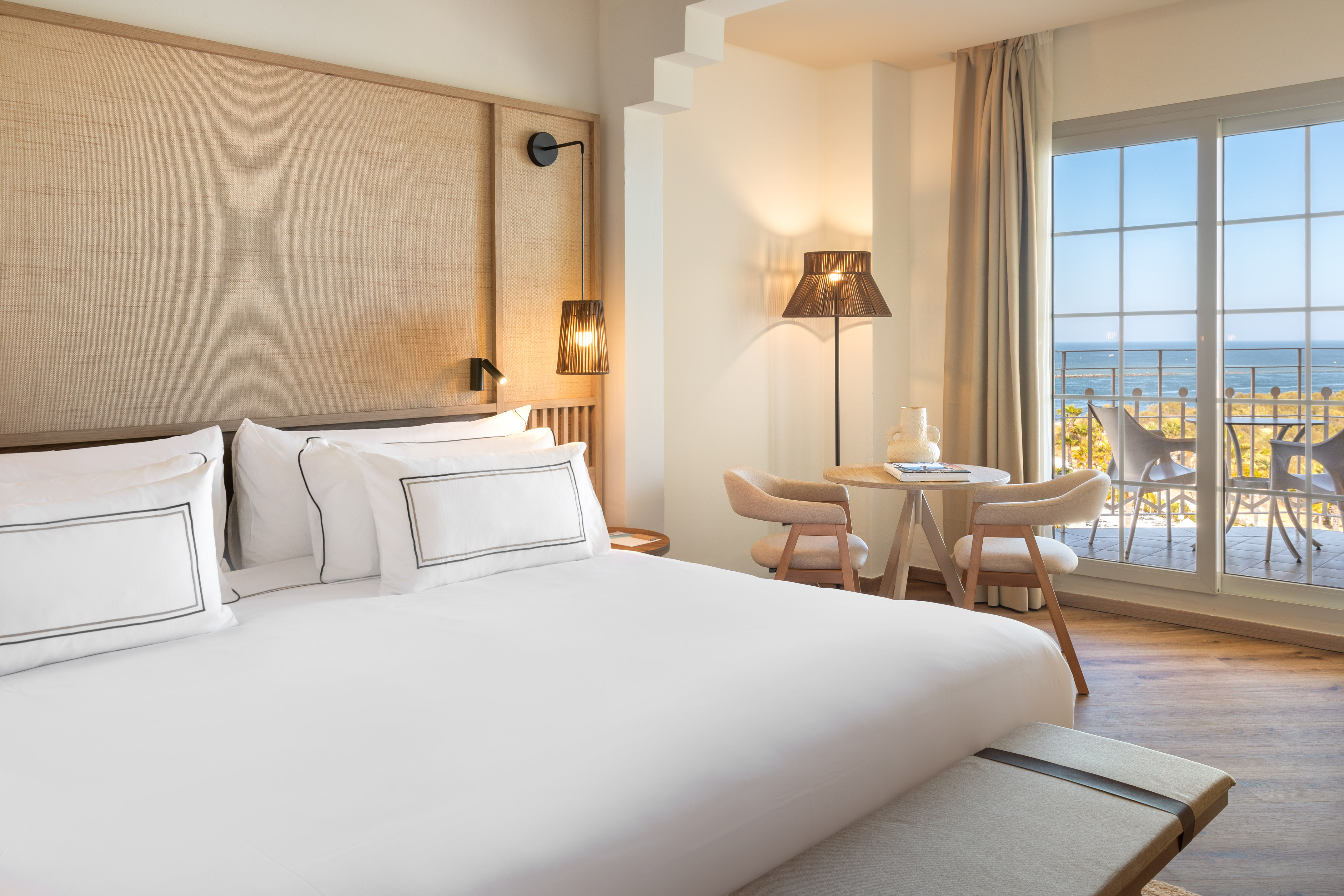 Hotel bedroom with white bed, ocean view balcony, and modern decor.