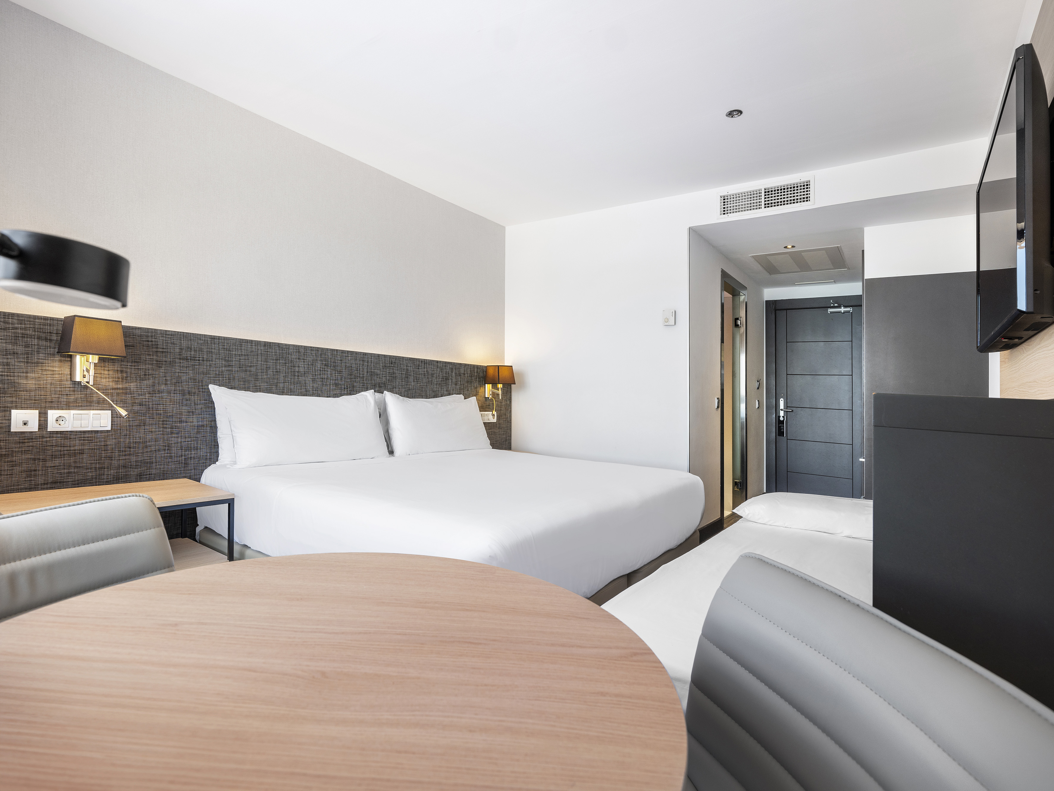 Modern hotel room with large bed, round table, and wall-mounted TV.