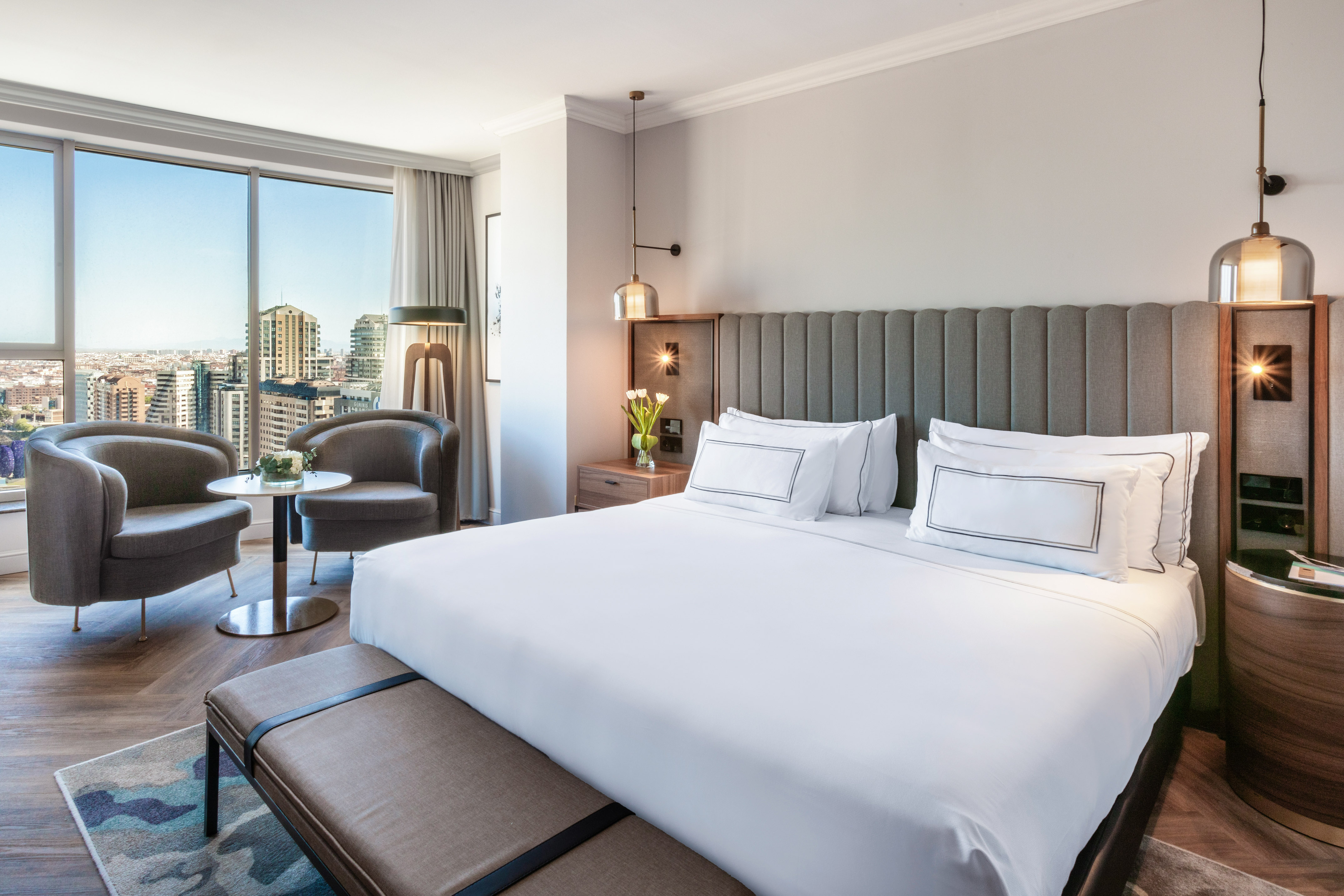 Luxury hotel room with king bed, city view, and armchairs by window.