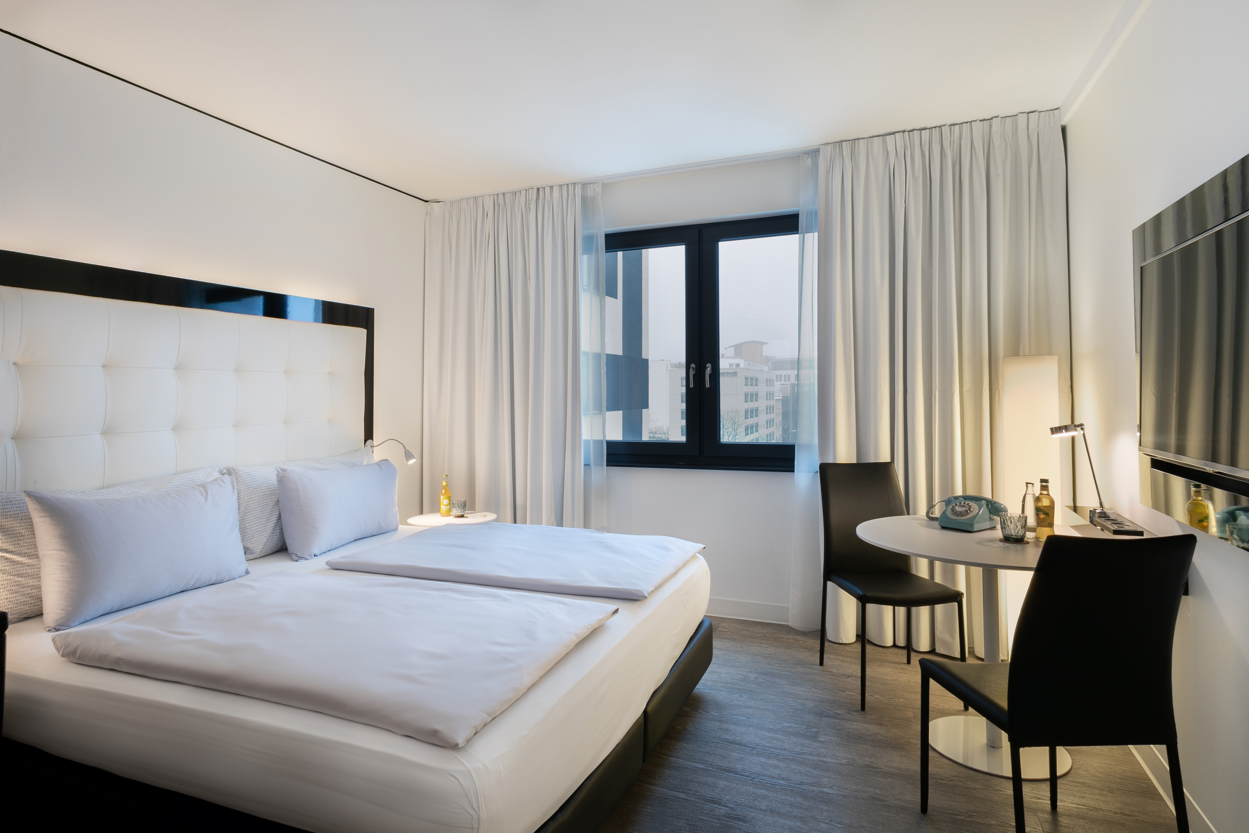 Modern hotel room with king bed, city view, and minimalist decor.