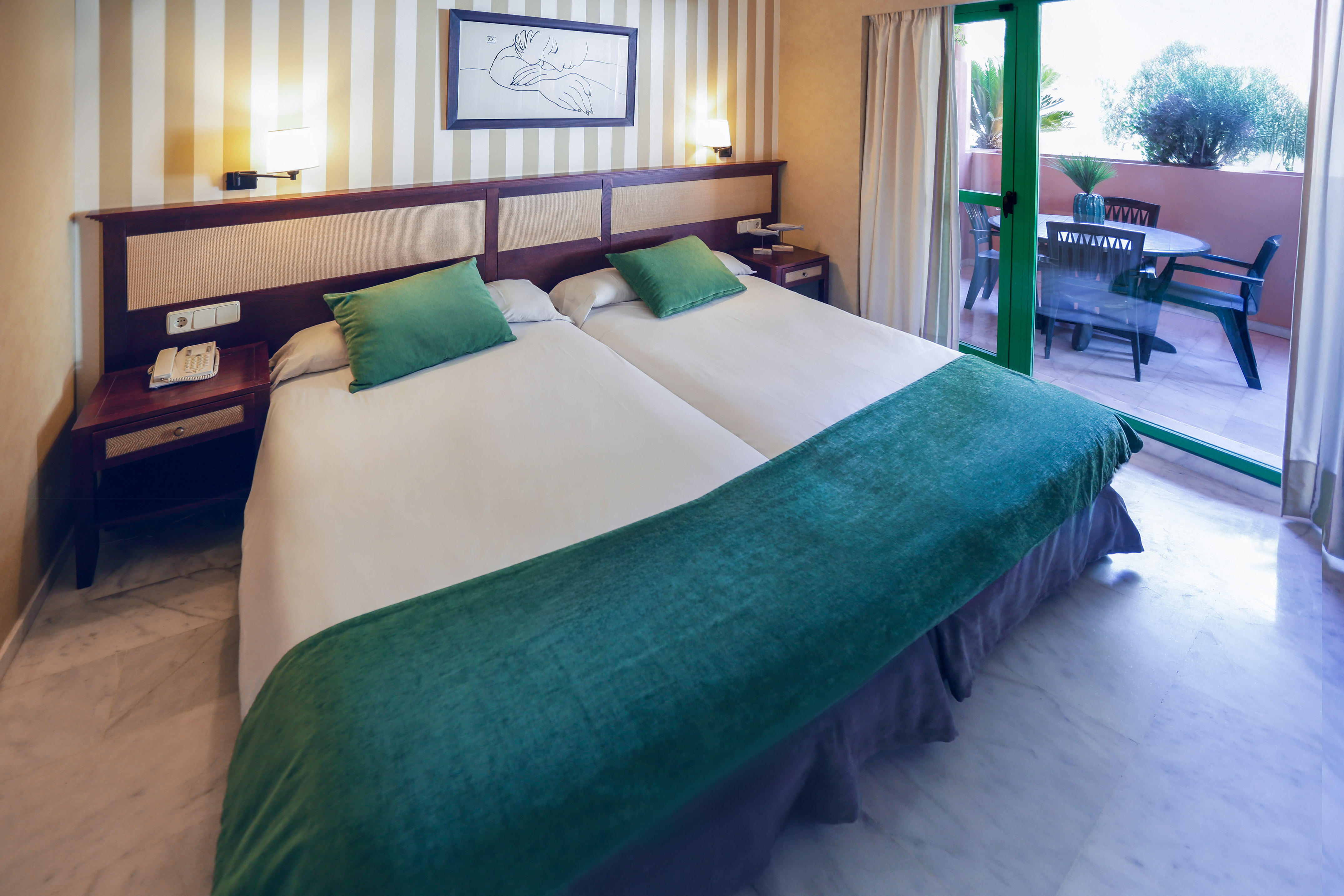 Hotel room with twin beds, green bedding, and a balcony with outdoor furniture.