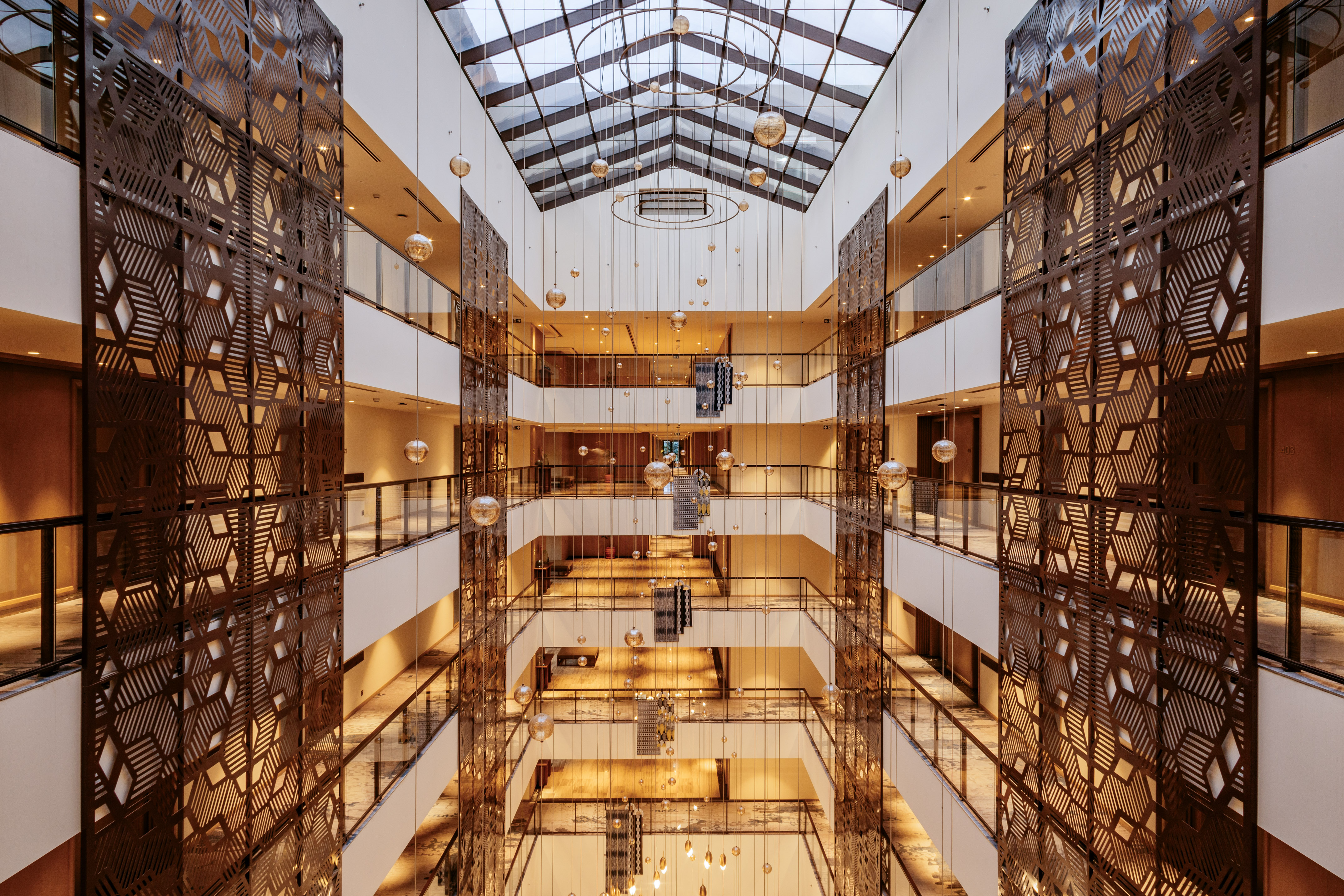 Modern hotel atrium with skylight, hanging spheres, and patterned metal screens.