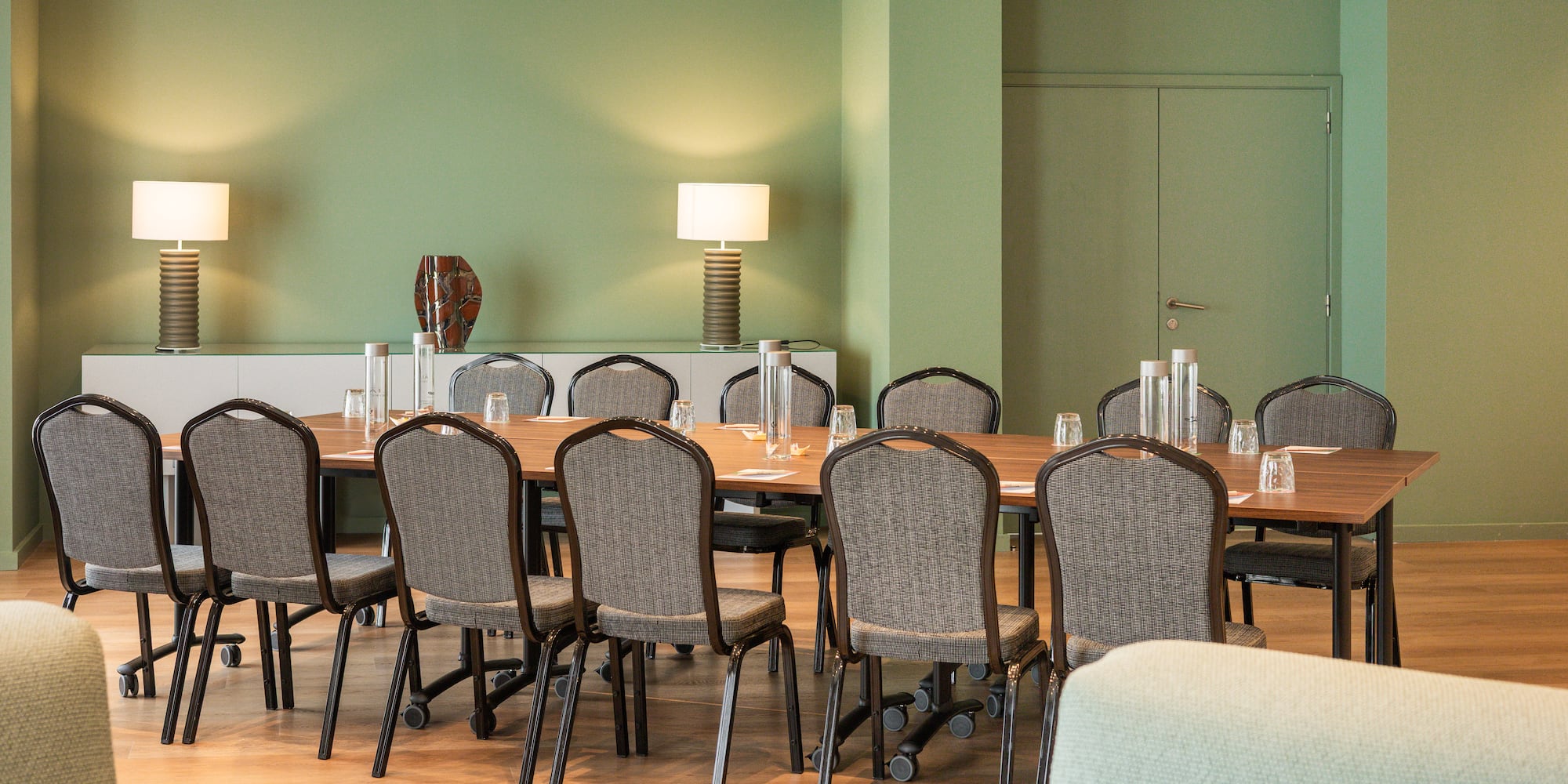 Professional meeting room with green walls, long wooden table, and chairs.