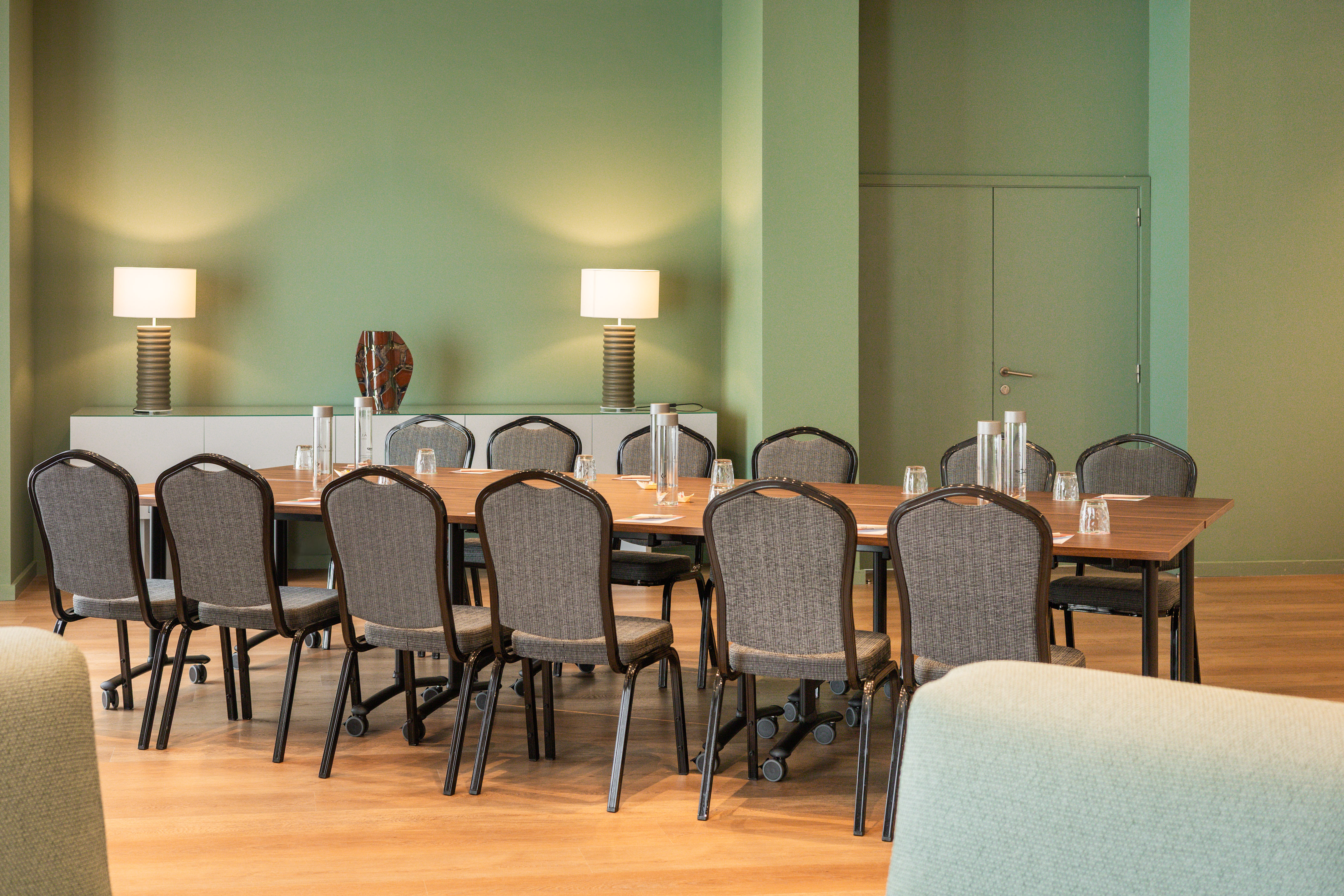 Professional meeting room with green walls, long wooden table, and chairs.