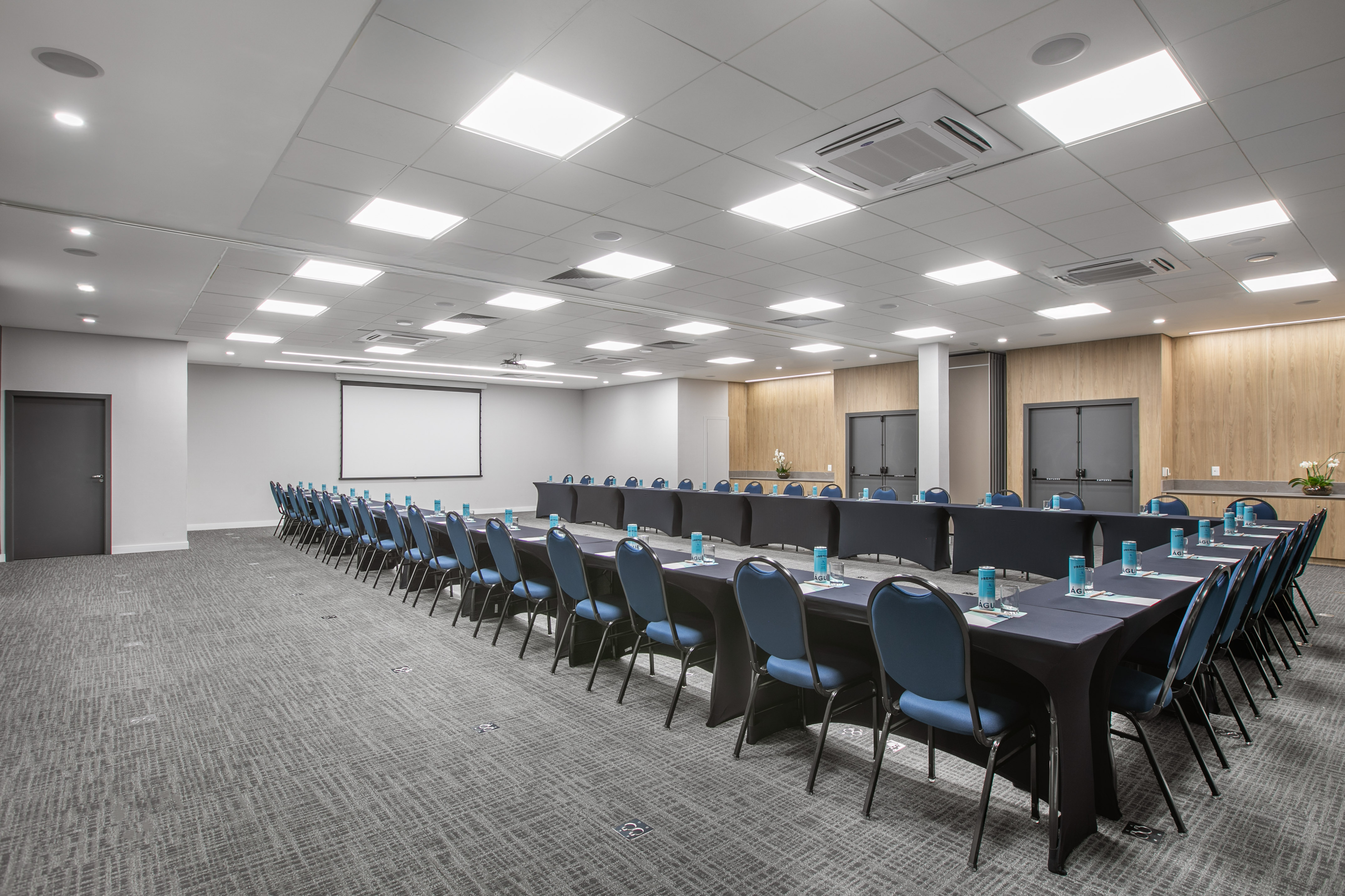 Professional conference room with U-shaped tables, blue chairs, projector screen.