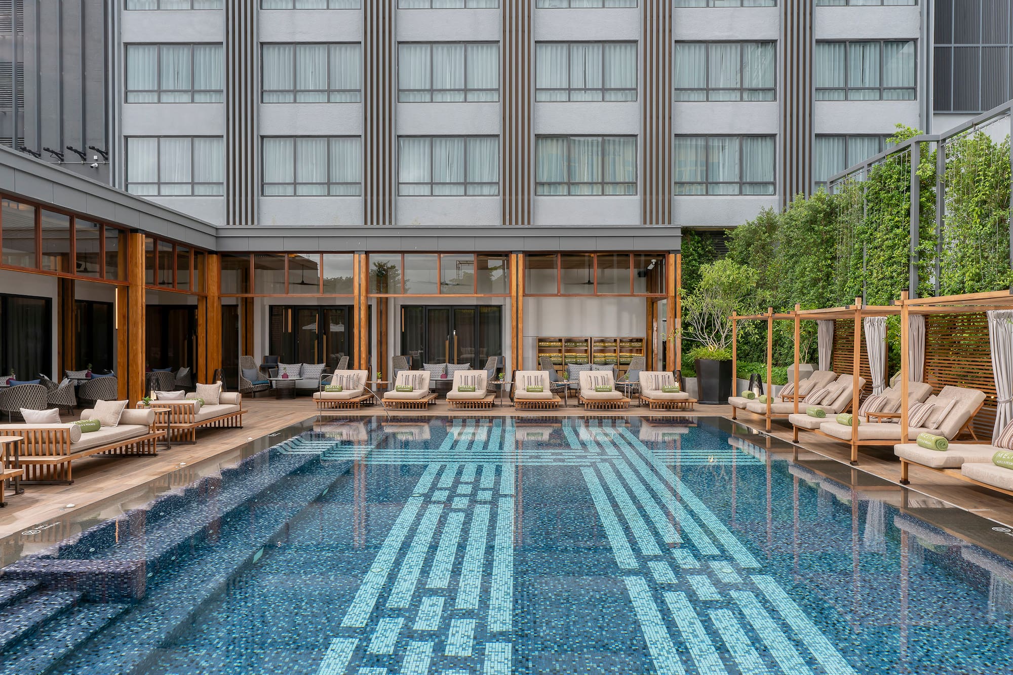 Modern resort pool with mosaic pattern, sun loungers, and hotel architecture.