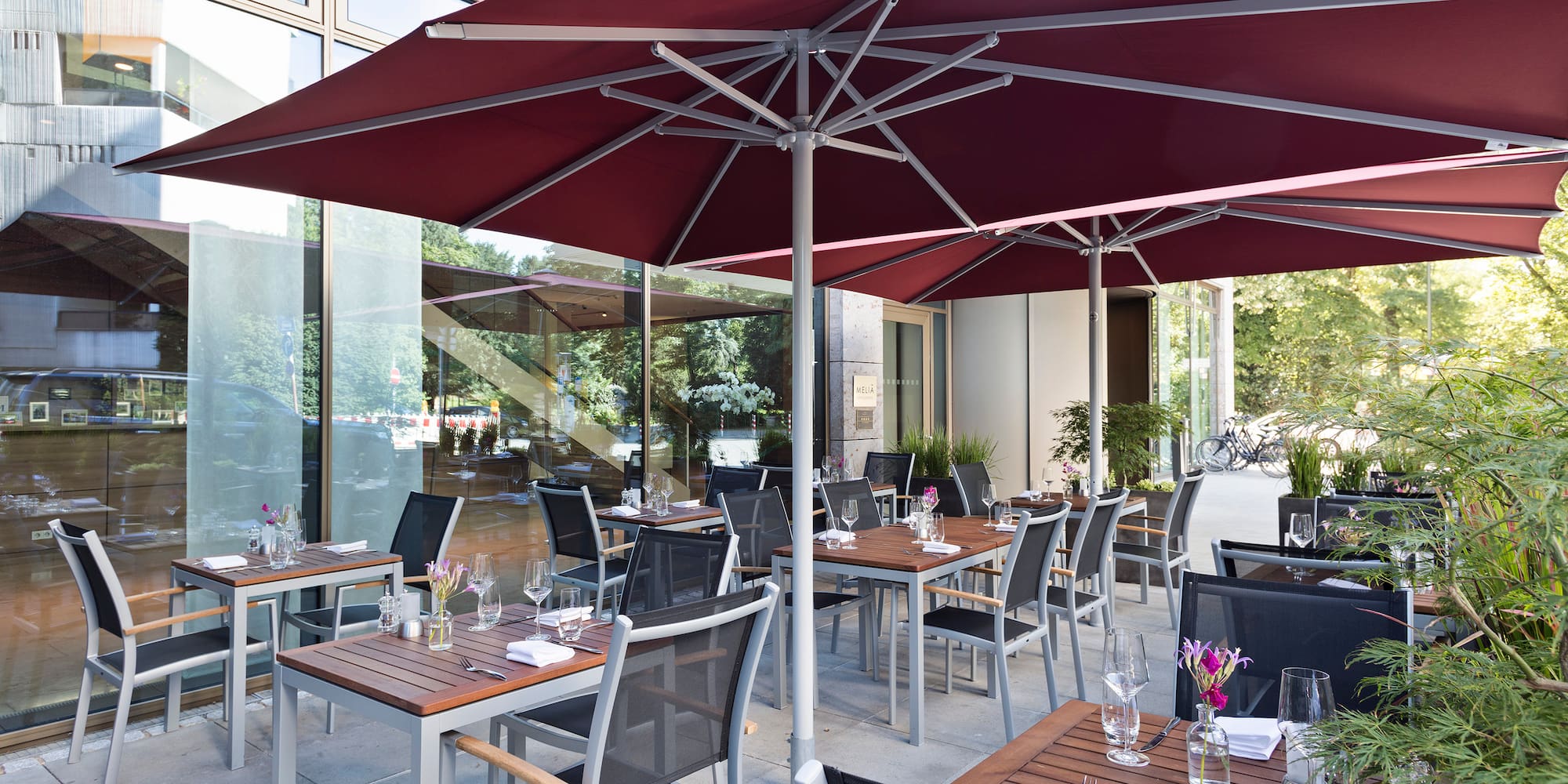 Meliá hotel outdoor restaurant patio with red umbrellas and set dining tables.