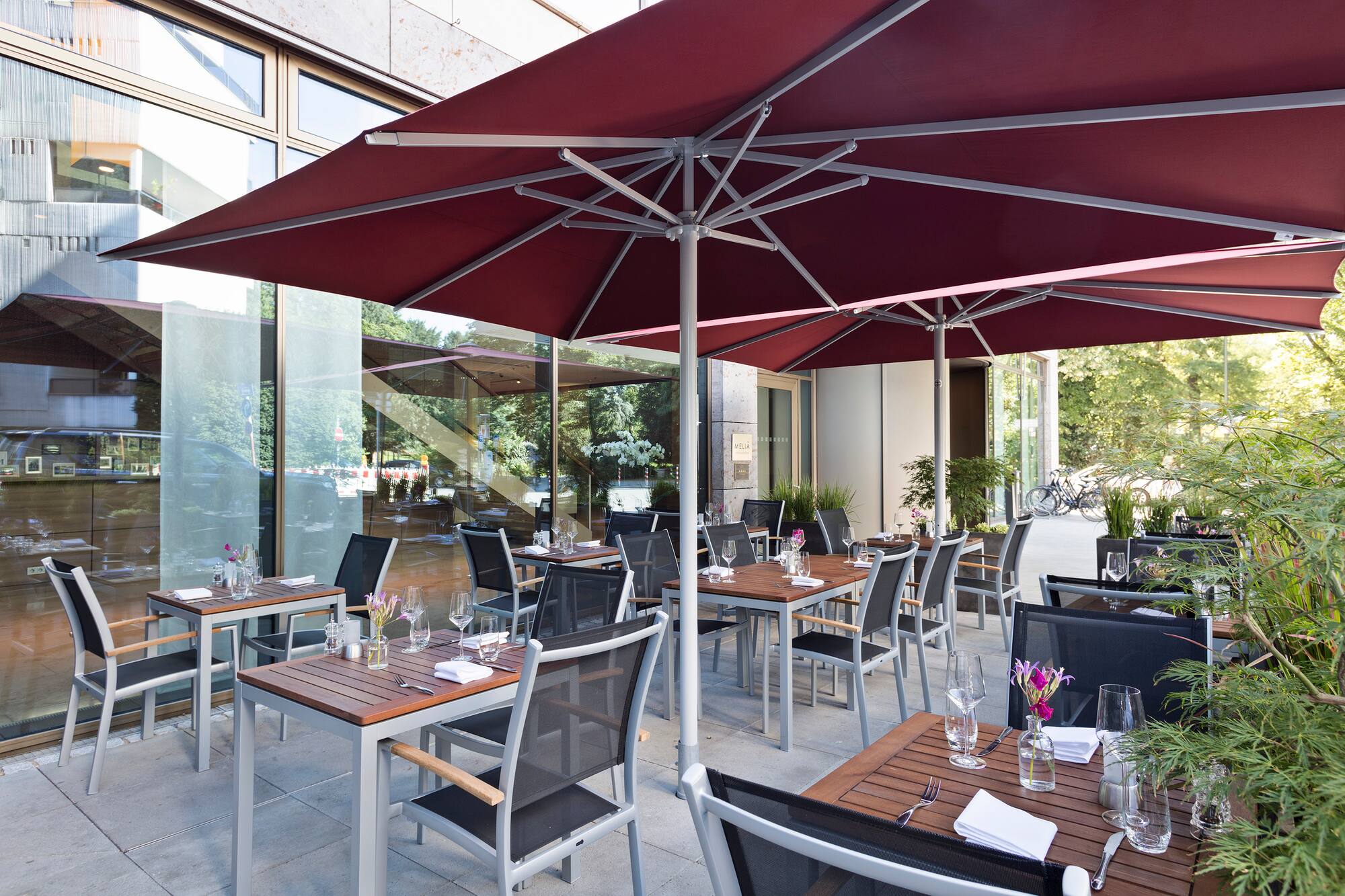 Meliá hotel outdoor restaurant patio with red umbrellas and set dining tables.